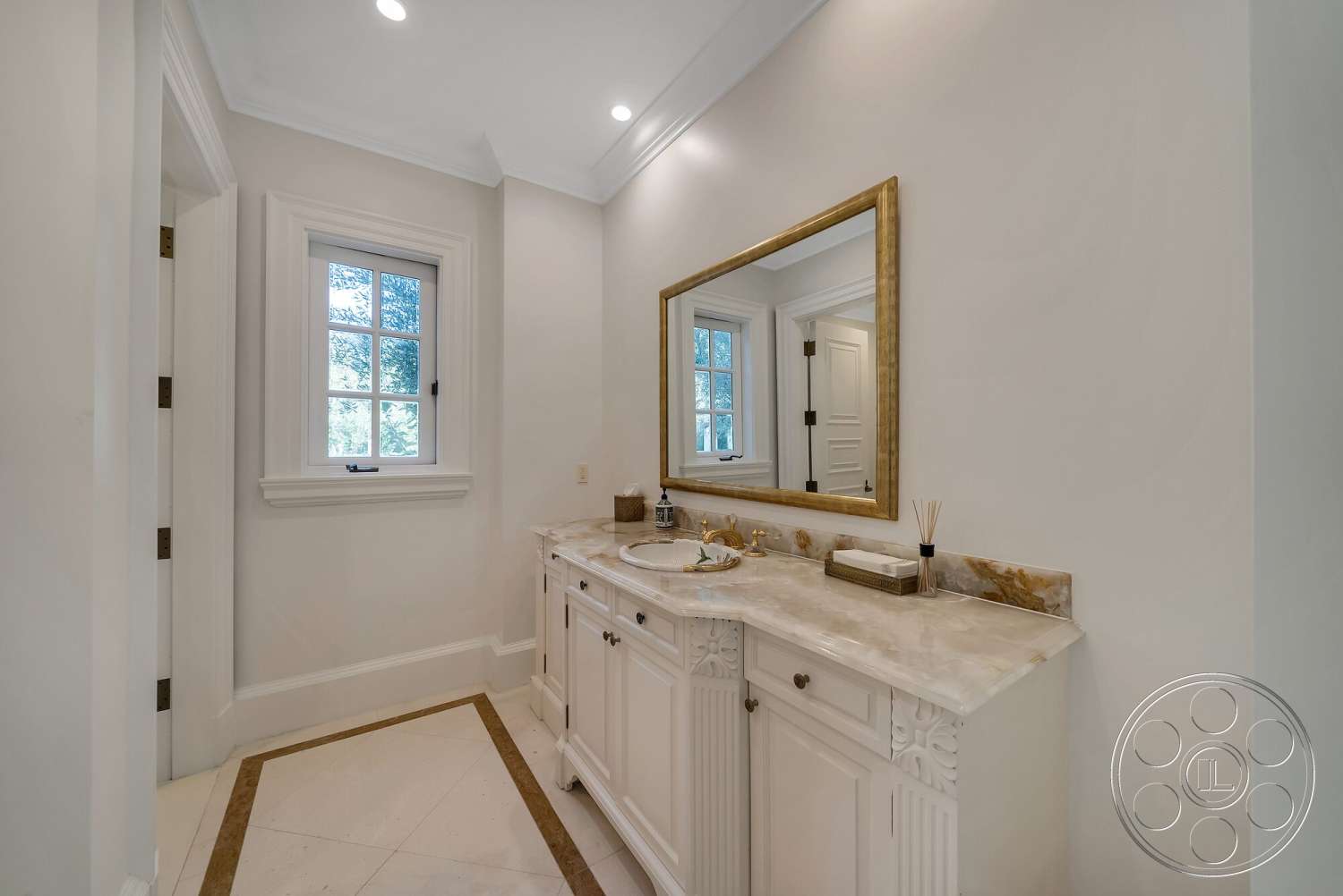 Medit 171 - white painted walls, gold-framed mirror, crown molding details, marble vanity countertop, double-hung window, white cabinetry with decorative details, tile bathroom flooring with decorative border