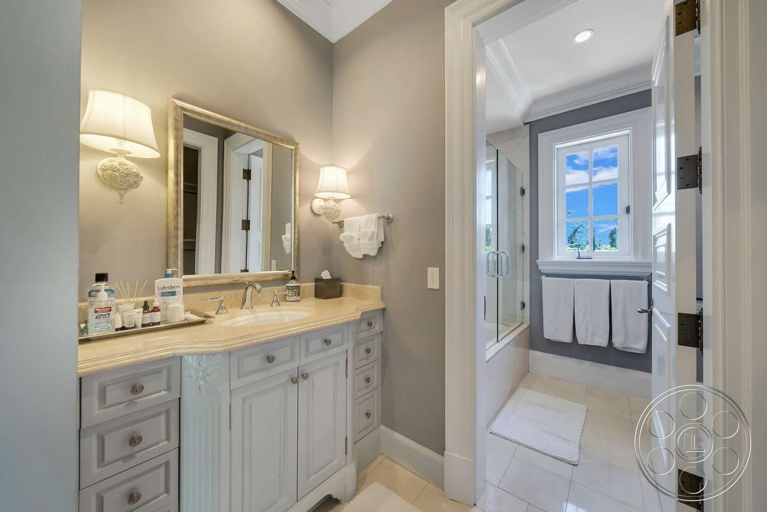 Medit 171 - glass shower enclosure, recessed ceiling lights, crown molding details, marble bathroom flooring, framed wall mirror, light gray painted walls, white trim details, large double-hung window, polished chrome faucet fixtures, double sink vanity with gray cabinetry, white bath towels, bathroom interior