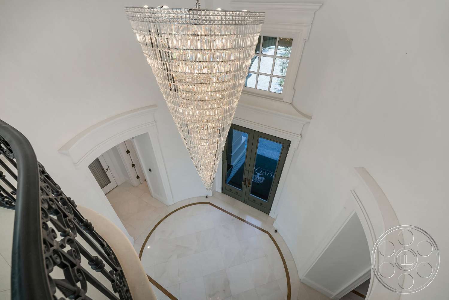 Medit 171 - chandelier lighting, arched entryway, white marble flooring, curved staircase, black wrought iron railing, neutral painted walls, intricate molding details, double entry doors, oval ceiling feature, decorative floor inlay