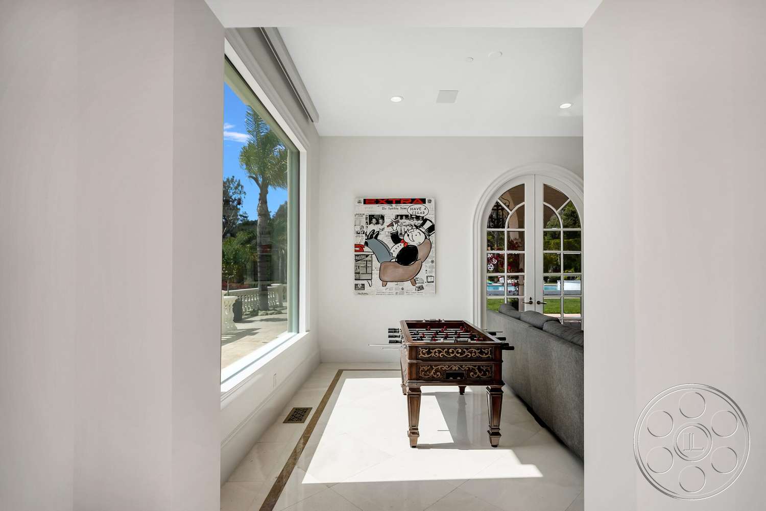Medit 171 - floor-to-ceiling windows, marble flooring, arched doorways, white painted walls, modern artwork display, elegant foyer space, traditional wooden foosball table, upholstered gray sofa