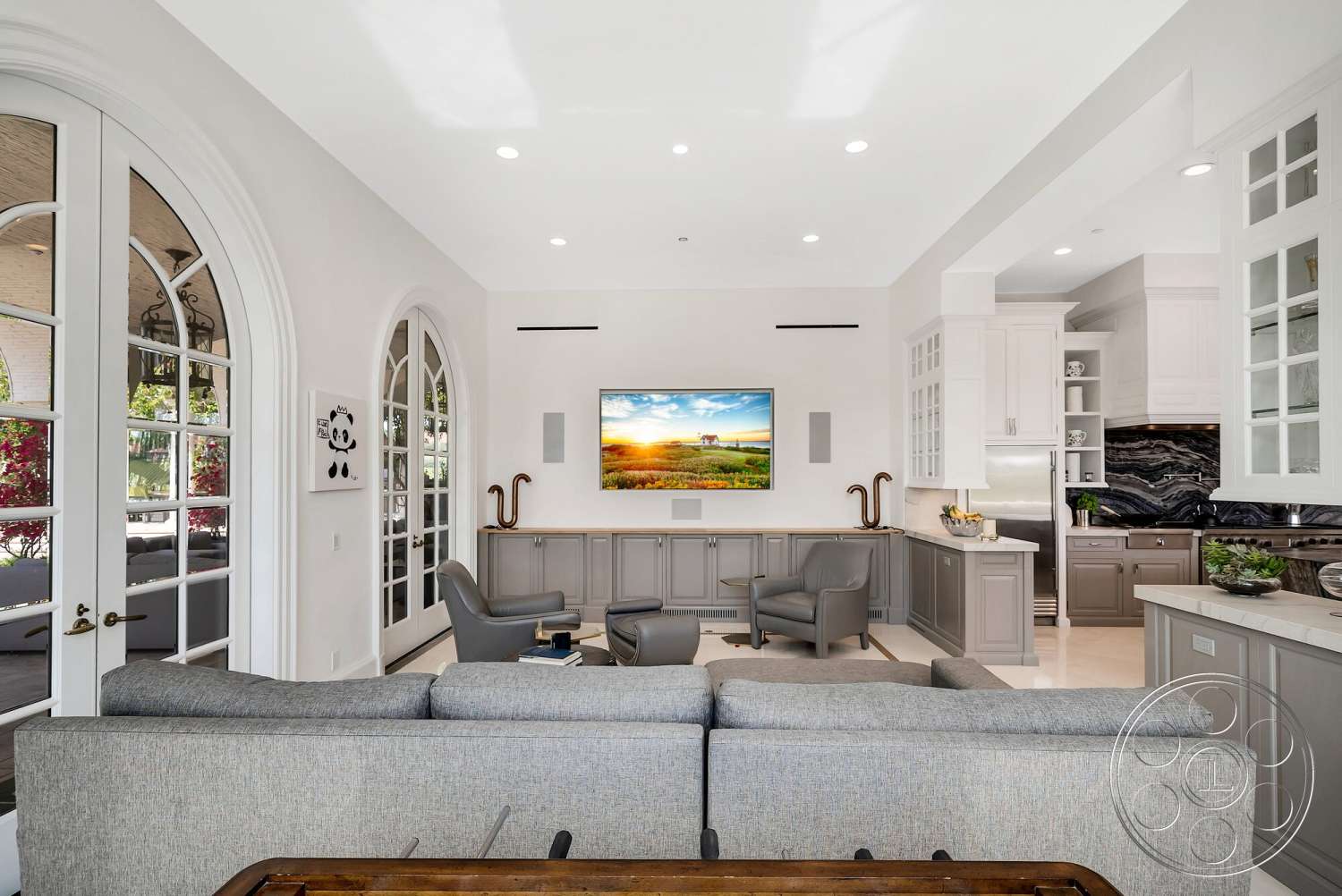 Medit 171 - wood coffee table, floor-to-ceiling windows, white cabinetry, decorative wall art, gray sectional sofa, television mounted on wall, formal dining area, light-colored tile flooring, black marble backsplash, neutral painted walls, high ceilings with recessed lighting, open-concept living room, modern gray armchairs, dark stone kitchen countertop, glass-front upper cabinets, arched double door entry