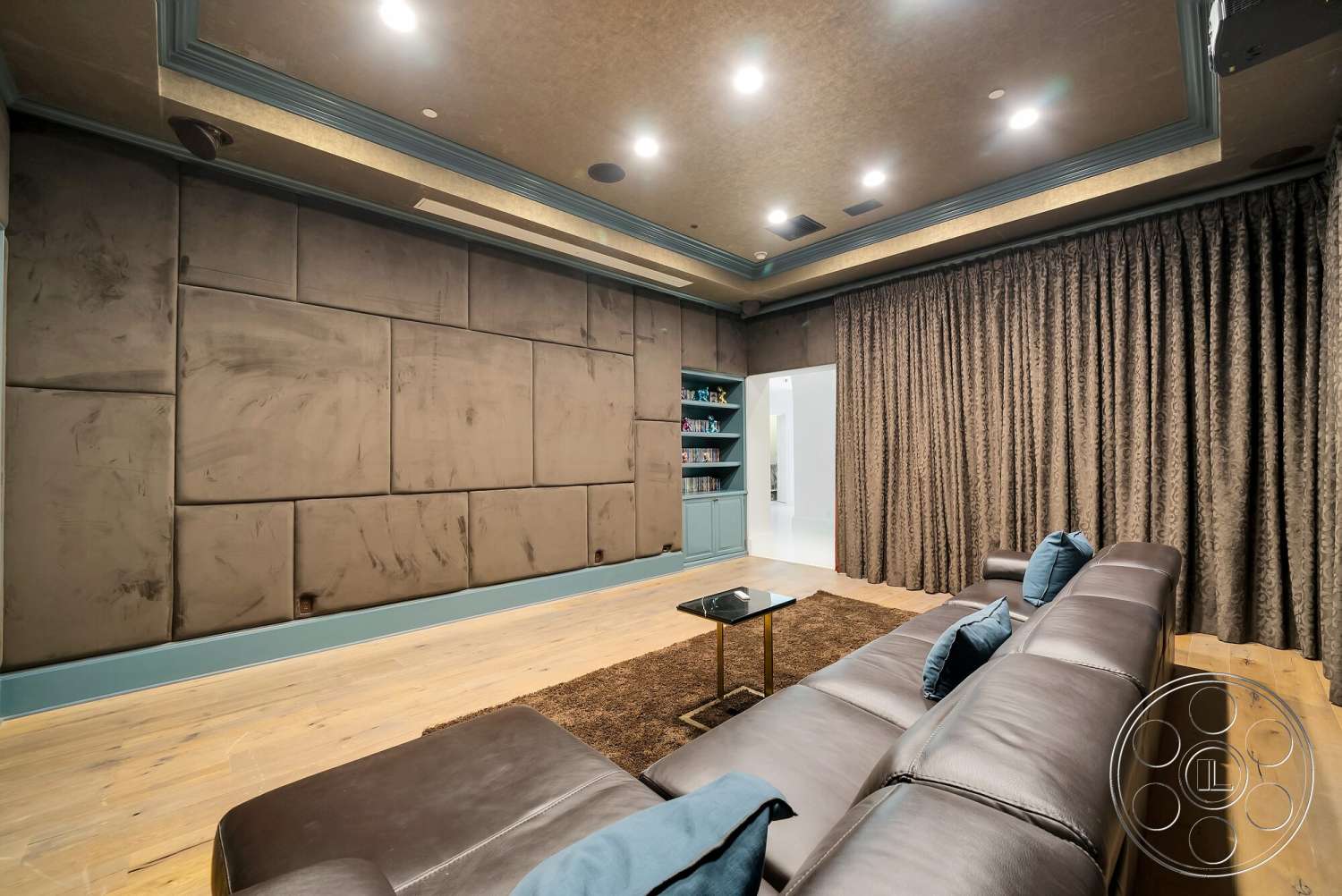 Medit 171 - dark wood cabinetry, blue accent pillows, tan area rug, textured plaster wall, soft recessed lighting, wood paneling ceiling, chocolate brown leather sectional sofa, gold accent coffee table, curtains with a rich texture, entertainment room