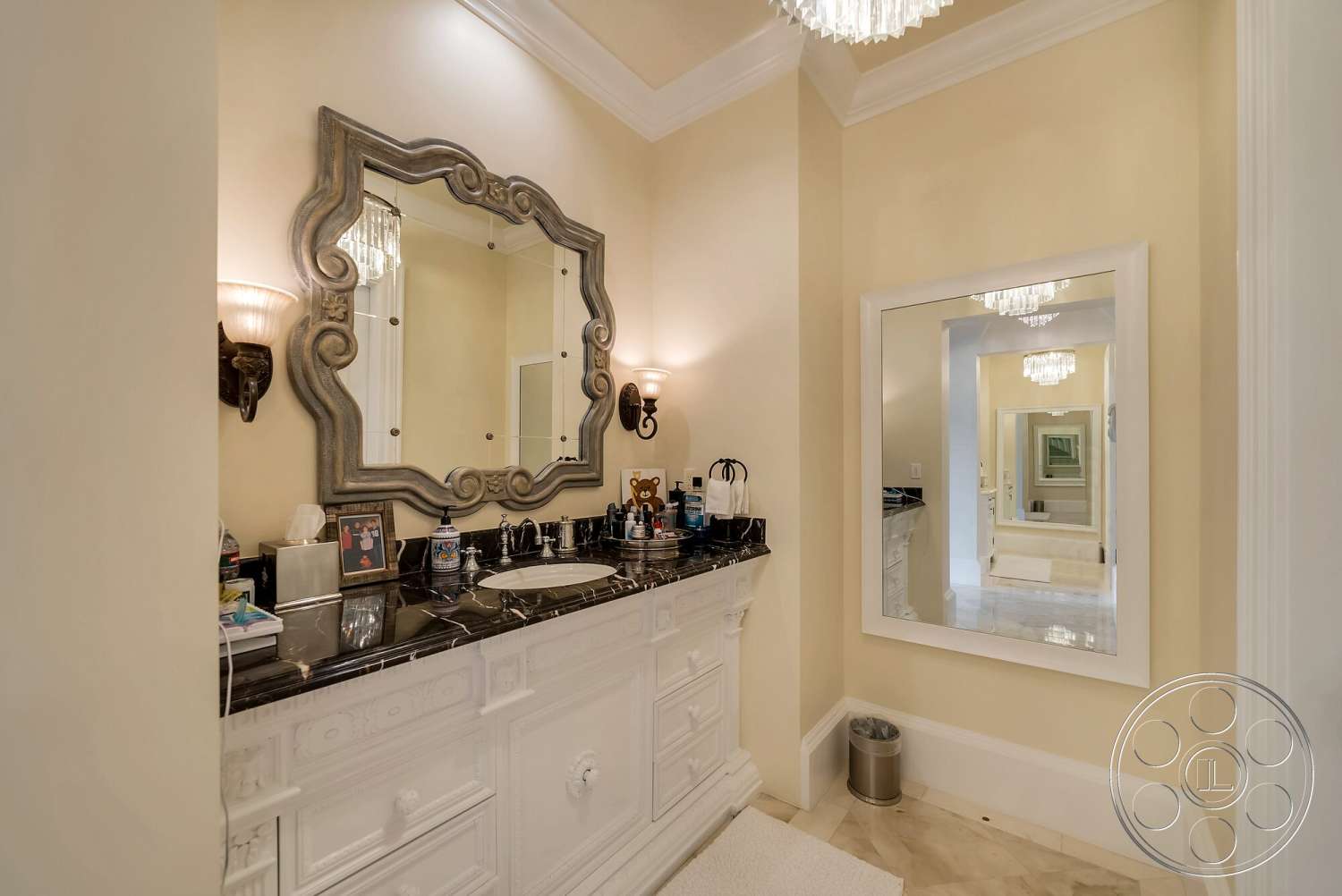 Medit 171 - cream-colored walls, textured plaster walls, black granite countertop, floor-to-ceiling mirror, luxury chandelier lighting, marble bathroom flooring, intricate crown molding details, ornate wall mirror, white decorative cabinetry, chrome wall sconces, neutral bathroom rug