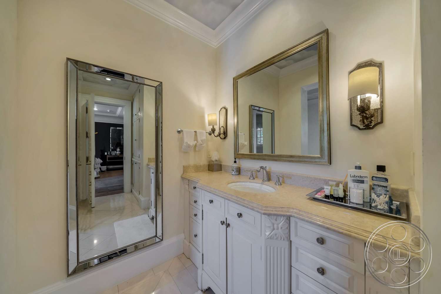 Medit 171 - light beige countertop, textured plaster walls, wall-mounted sconces, crown molding details, marble bathroom flooring, framed wall mirror, elegant room design, white cabinet vanity with decorative details, sink with polished chrome faucet, luxurious bathroom environment