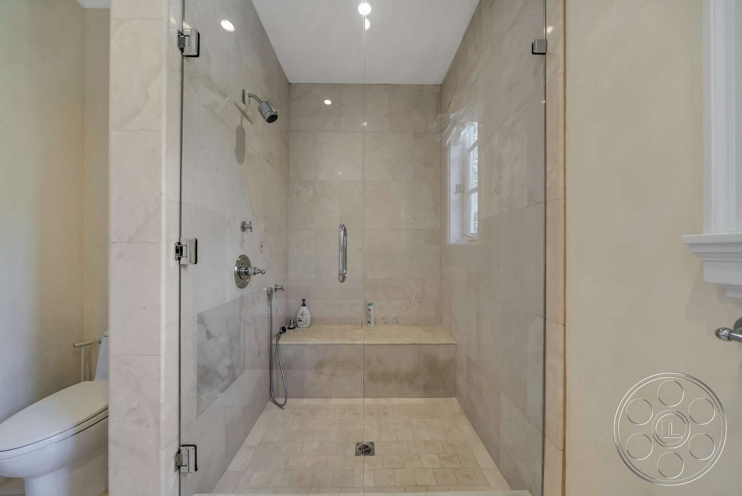 Medit 171 - white toilet, natural light from windows, glass shower doors, chrome shower fixtures, neutral painted walls, built-in shower bench, interior marble shower flooring, interior stone shower walls
