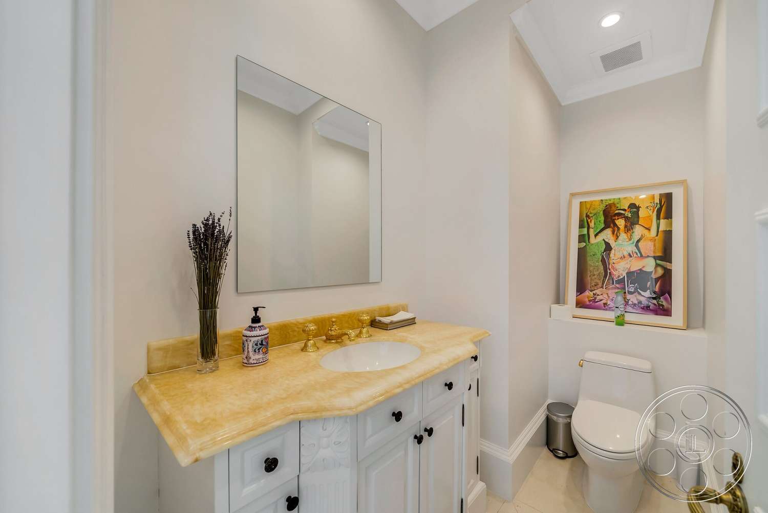 Medit 171 - tile flooring, framed artwork, recessed ceiling lighting, white painted walls, modern art piece on wall, porcelain toilet, large wall mirror, stone vanity countertop, black and white cabinet details, lavender floral arrangement, drop-down ceiling with molding