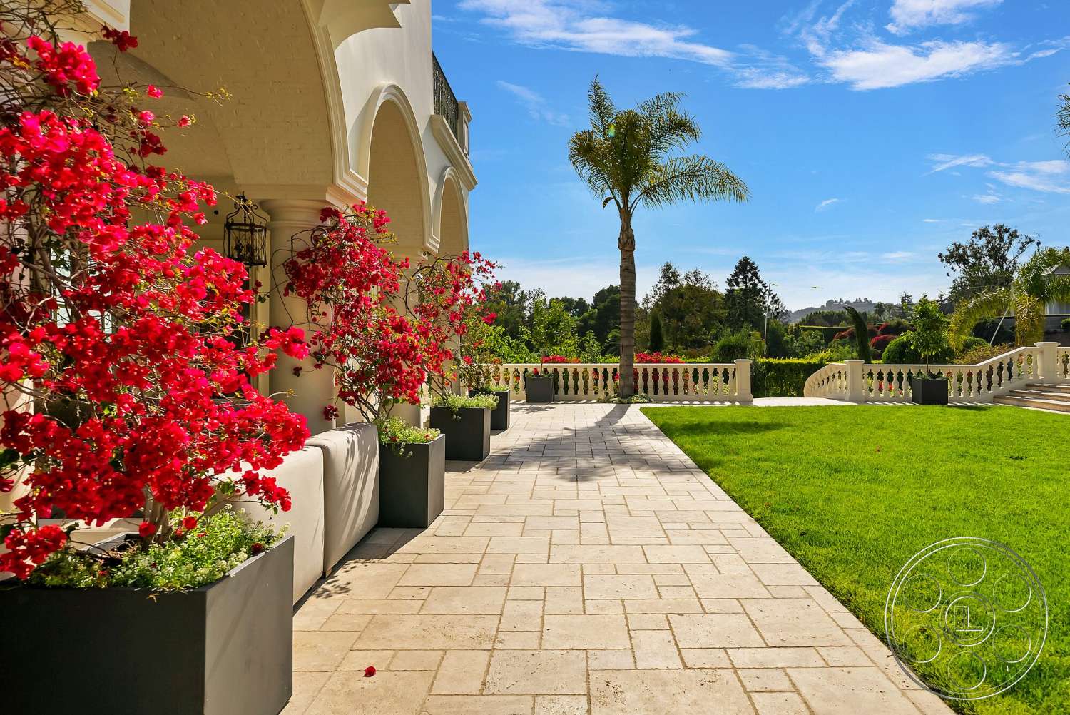Medit 171 - exterior, landscaped garden, lawn area, tropical palm trees, sunny outdoor setting, curved garden path, decorative stone railing, decorative planter boxes, open sky backdrop, travertine stone patio flooring, vibrant bougainvillea flowers, arched architectural details