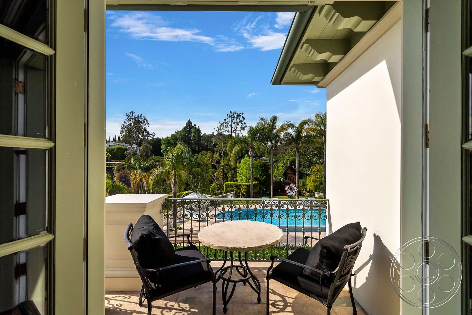 Medit 171 - exterior, landscaped garden view, round dining table, tropical palm trees, modern outdoor seating, bright blue sky, stone patio flooring, wrought iron balcony railings, concrete swimming pool, wooden ceiling overhang, elegant exterior architecture