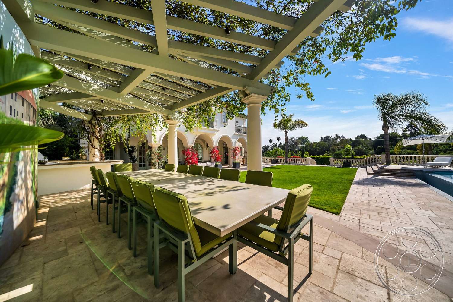 Medit 171 - exterior, outdoor dining area, paved walkway, landscaped lawn, arched openings, residential pool area, sunny outdoor setting, stone patio flooring, concrete dining table, pergola with wooden beams, green outdoor chairs, lush garden with palm trees, brick wall with painted mural