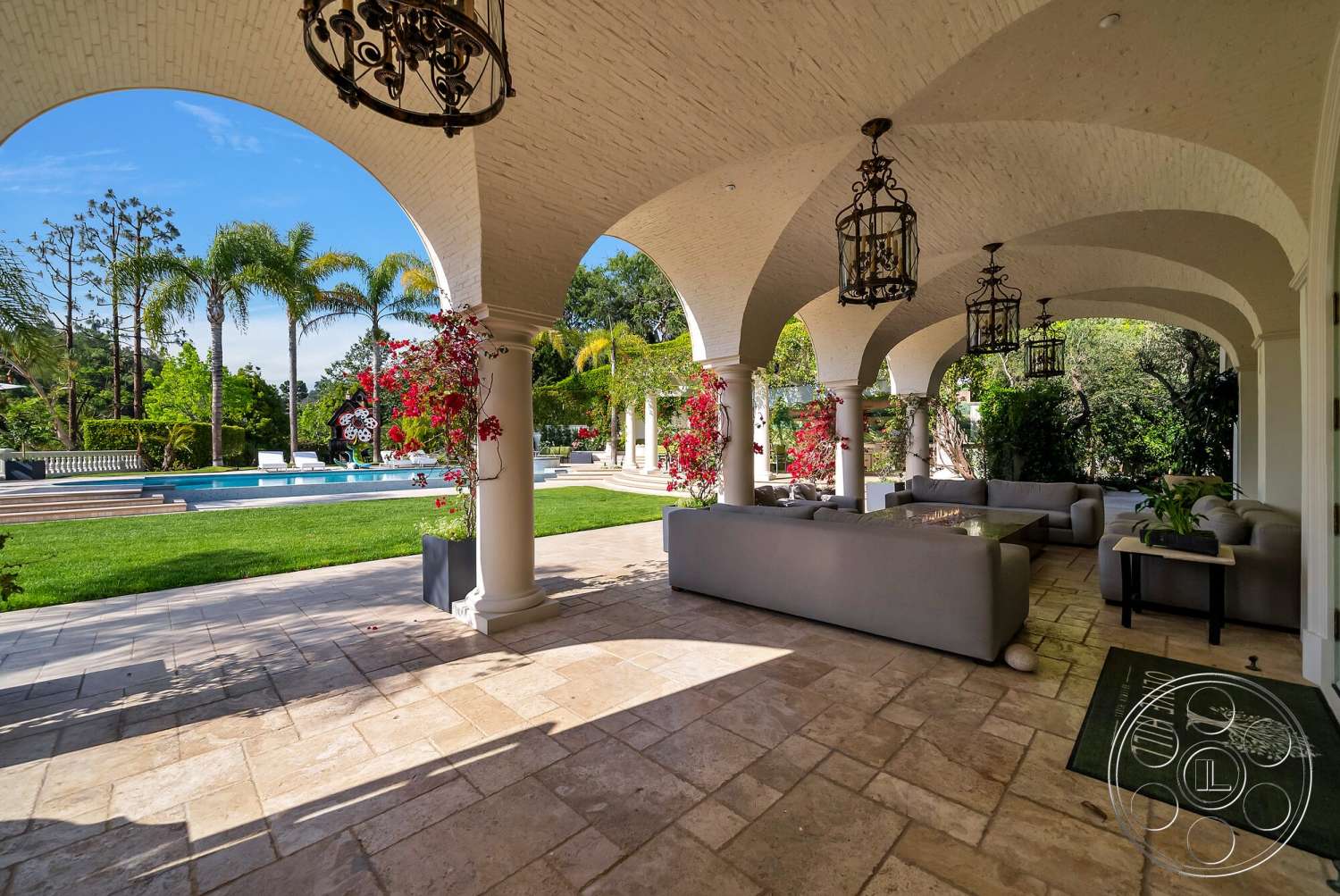 Medit 171 - exterior, landscaped garden, textured plaster ceiling, floral accents, green grass lawn, arched columns, contemporary outdoor seating, lush palm trees, natural stone patio flooring, decorative hanging lanterns, swimming pool with deck