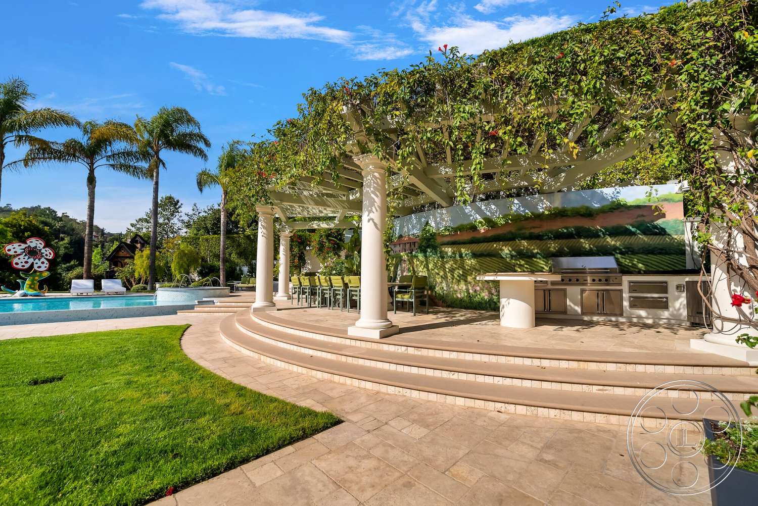 Medit 171 - exterior, rectangular swimming pool, outdoor dining space, tropical palm trees, outdoor kitchen area, wood pergola structure, stone patio flooring, built-in stainless steel grill, curved steps, grassy landscape, column-supported roof, green trellised vines, scenic vineyard mural backdrop