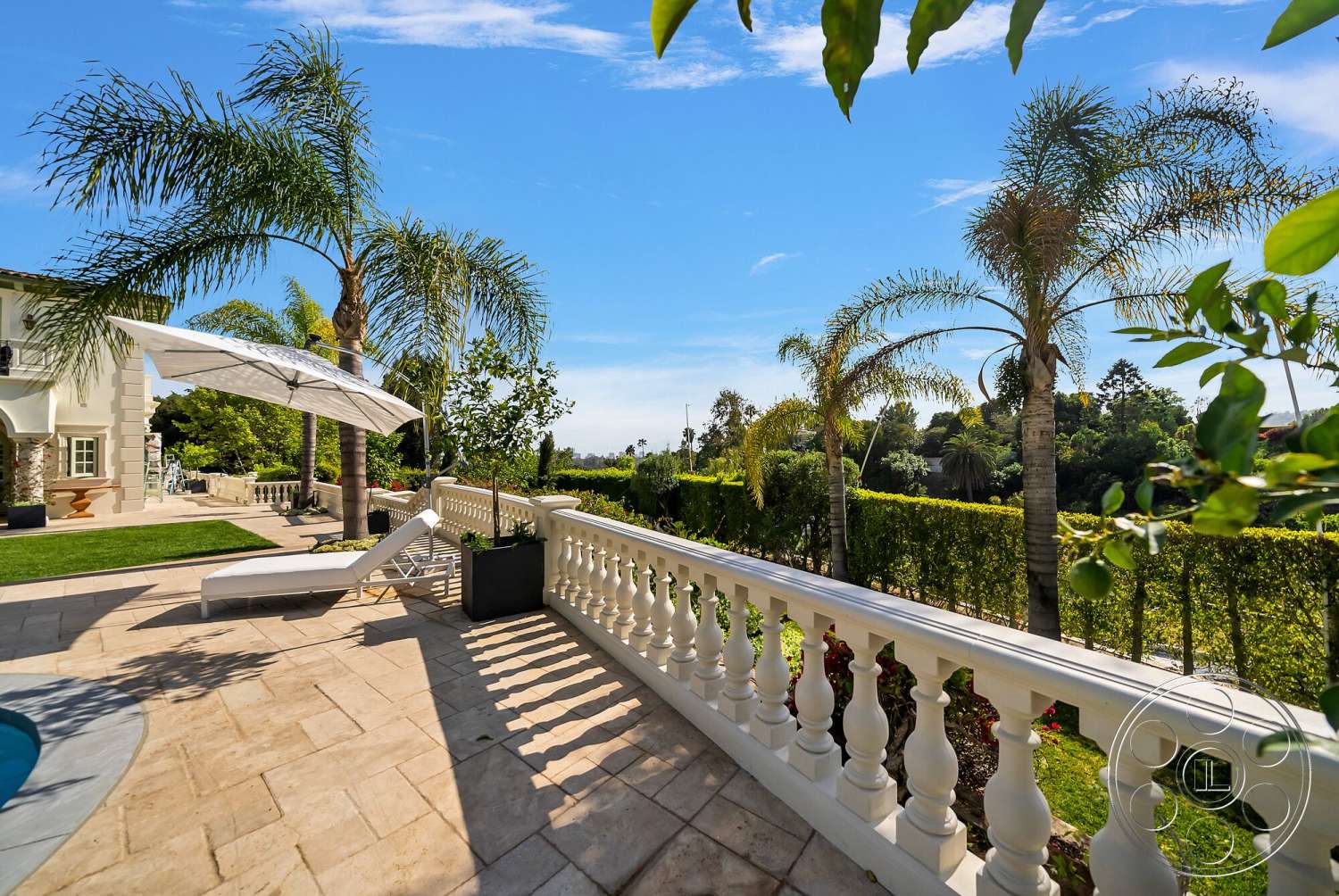 Medit 171 - exterior, rectangular swimming pool, clear blue sky, green grass lawn, hedge privacy fence, outdoor umbrella, stone patio flooring, palm trees landscaping, white painted railing, sun lounge chair