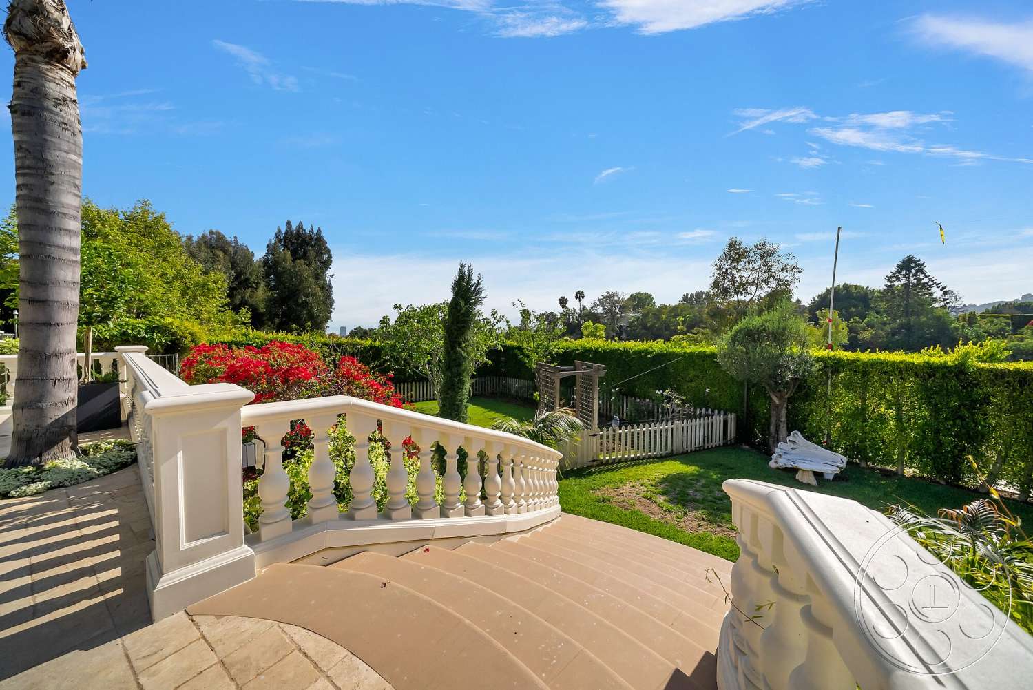 Medit 171 - exterior, lush greenery, green lawn, paved walkway, blue sky, tall palm trees, gentle slope, curved concrete steps, wooden garden fence, landscaped garden with flowering shrubs, ornate white railing, trellis feature