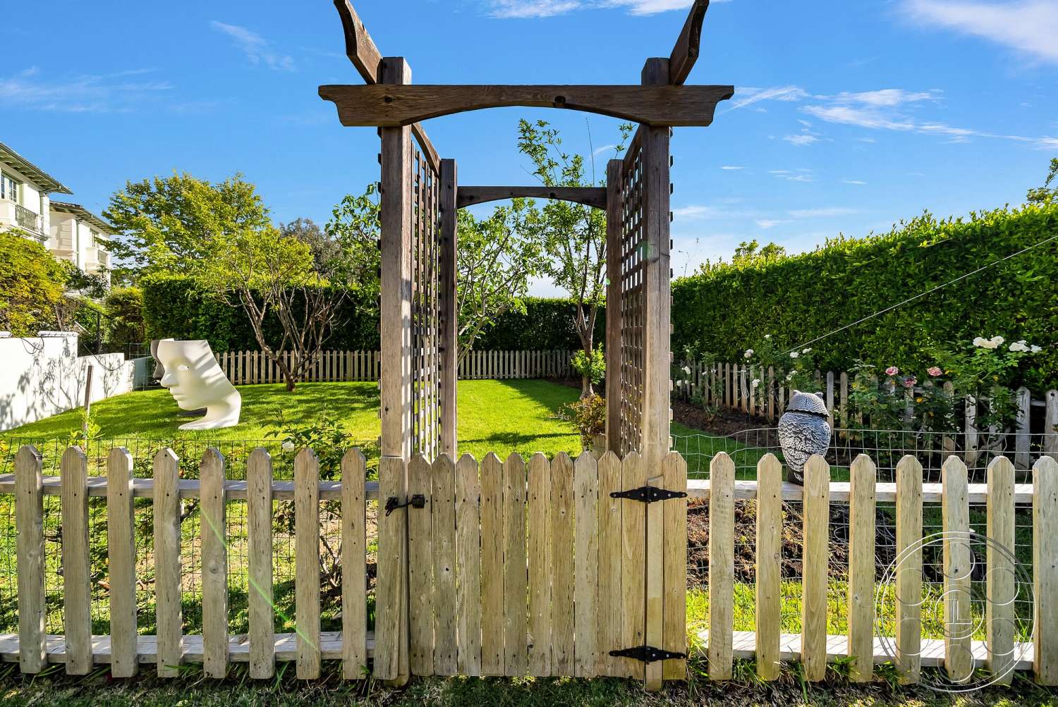 Medit 171 - outdoor garden setting, flower garden beds, green shrubbery backdrop, wood garden arbor, lattice fence panels, painted wood picket fence, freshly mown grass lawn, modern sculptural garden art, cleared garden path, bright sunny exterior