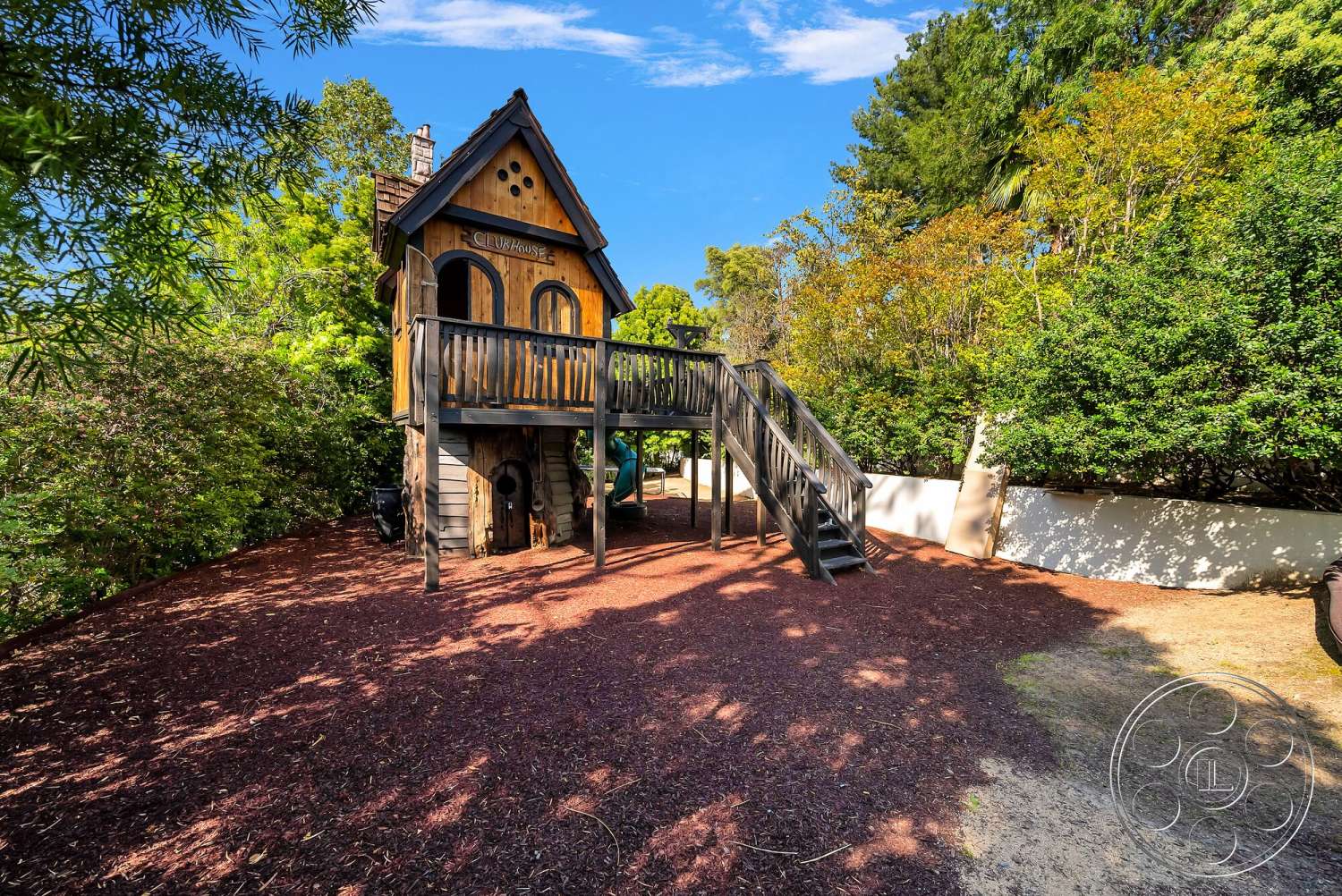 Medit 171 - surrounding greenery, arched windows, outdoor play area, natural wood siding, shingled roof, wooden playhouse exterior, raised wooden deck, stairs leading to deck, mulch playground surface, rustic style playhouse