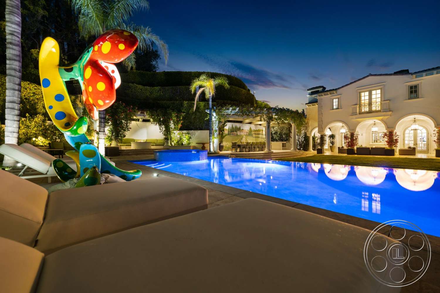 Medit 171 - exterior, palm trees, large glass windows, rectangular swimming pool, nighttime ambiance, modern outdoor seating area, concrete pool border, natural stone patio flooring, arced landscaping with hedges, decorative art sculpture, outdoor dining area with pergola, white stucco home, under-lit pool