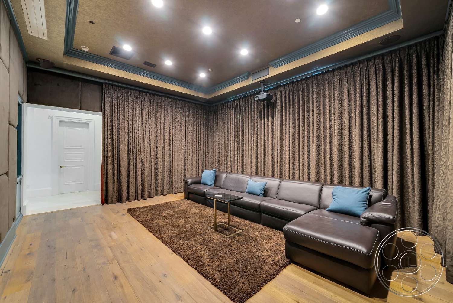 Medit 171 - hardwood flooring, blue accent pillows, projector system, leather sectional sofa, acoustic wall treatment, white paneled door, plush brown area rug, dark brown curtains, coffered ceiling with detailed molding, hidden speaker installation