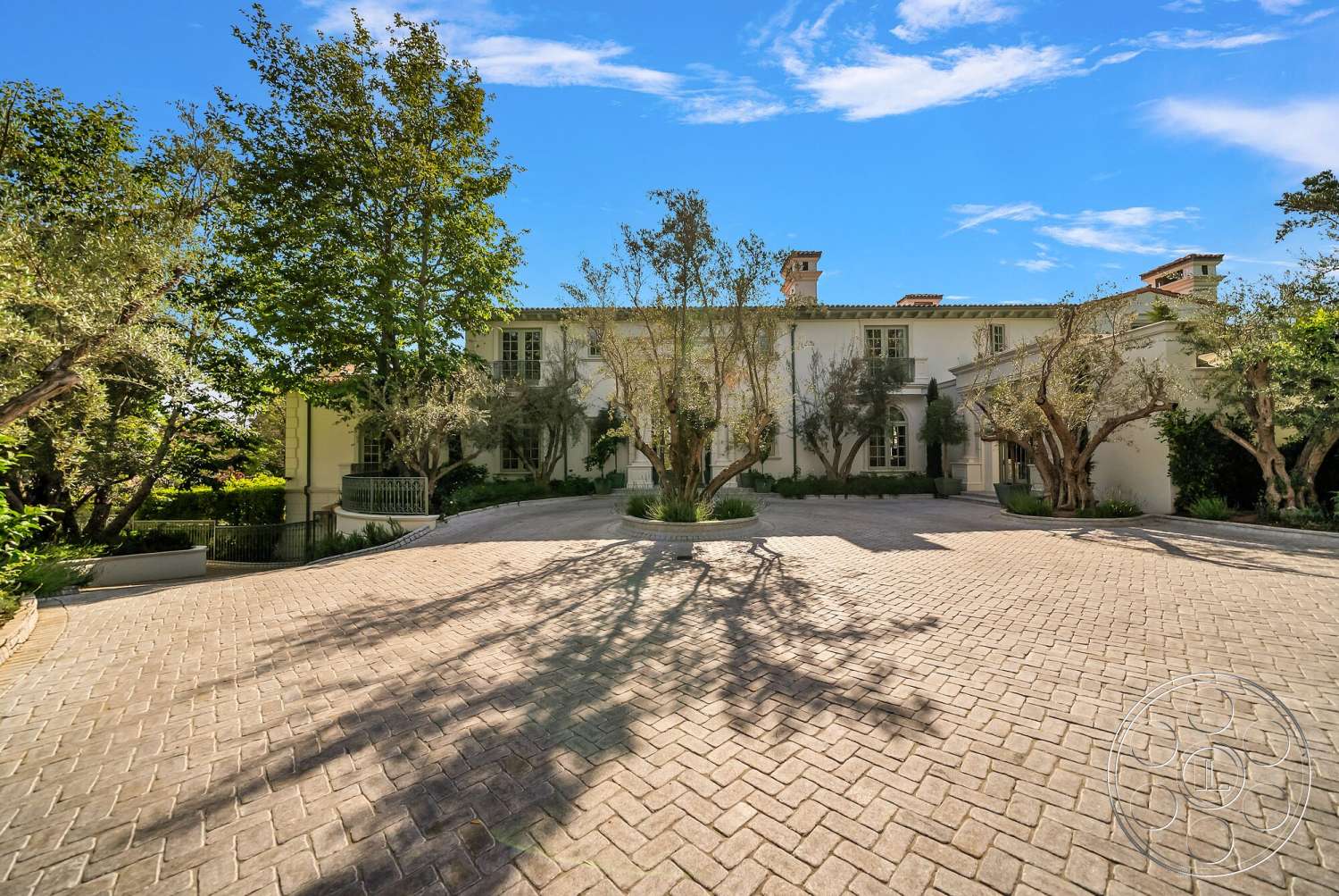 Medit 171 - white stucco walls, mountain view, spacious outdoor area, formal entryway, mature olive trees, exterior stone facade, green landscaped garden, ornate wrought iron railings, large multi-paned windows, paved circular driveway, symmetrical home design, tiled roof with gables, brick herringbone pattern driveway, luxury estate setting