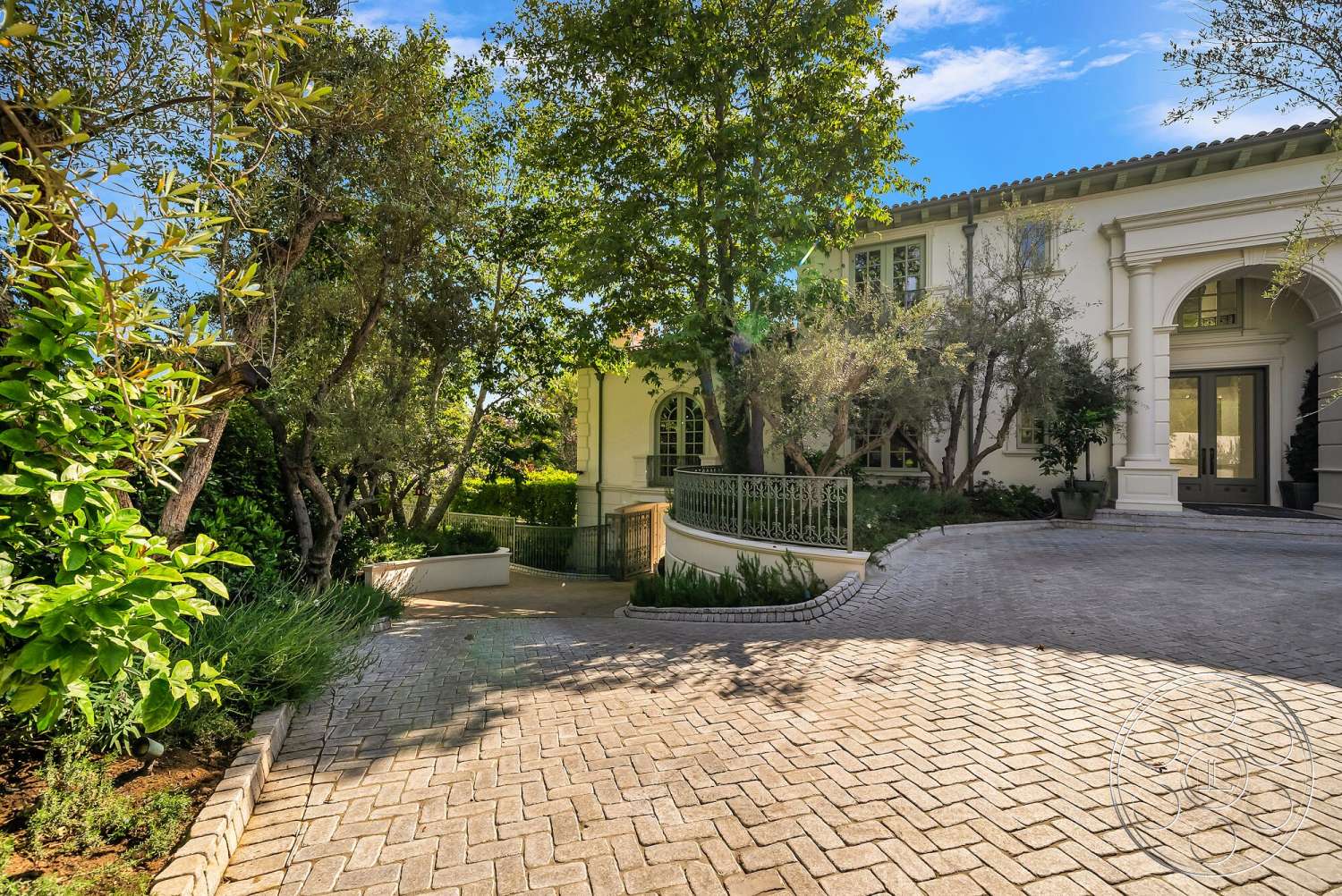 Medit 171 - paver driveway, concrete steps, curved driveway, arched entrance, Mediterranean architectural style, landscaped garden area, exterior stucco walls, large bay windows, iron railing fence, trees and shrubs landscape