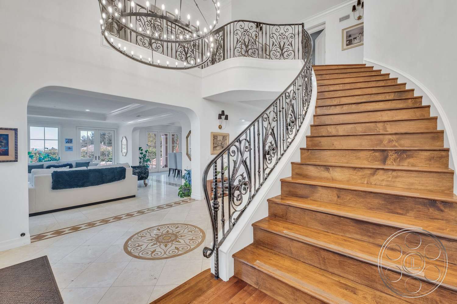 Medit 172 - neutral wall colors, large windows providing natural light, chandelier lighting fixture, wood staircase with iron railing, polished marble entryway flooring, arched doorways leading to living space, coffered ceiling details in living area, elegant decorative medallion in floor design