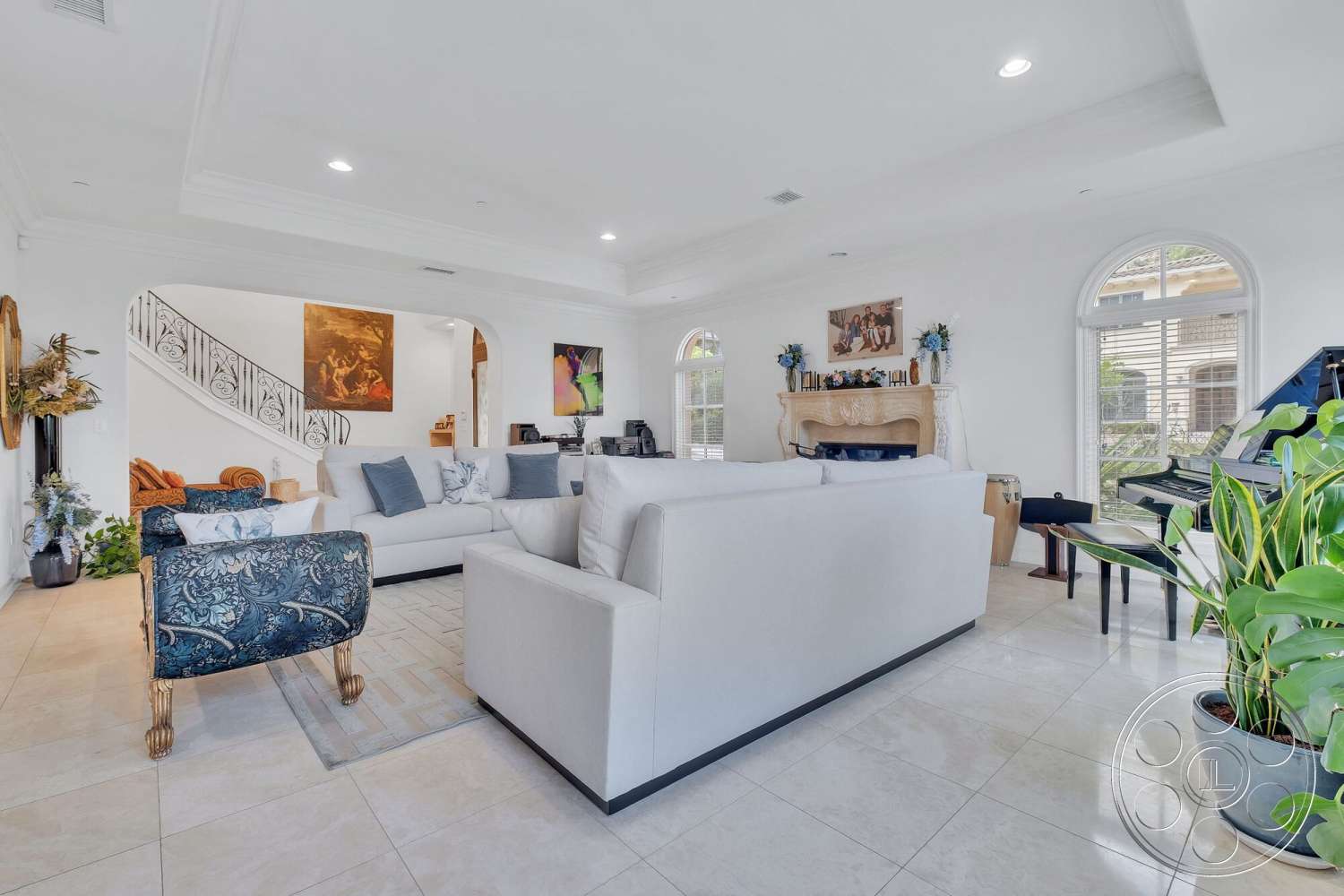 Medit 172 - indoor plants, decorative wall art, polished marble flooring, arched doorways, piano in corner, white painted walls, modern sectional sofa, large windows with decorative trim, stone fireplace surround, coffered ceiling details, open layout living area, accent chairs with floral upholstery, ornate staircase with wrought iron railing