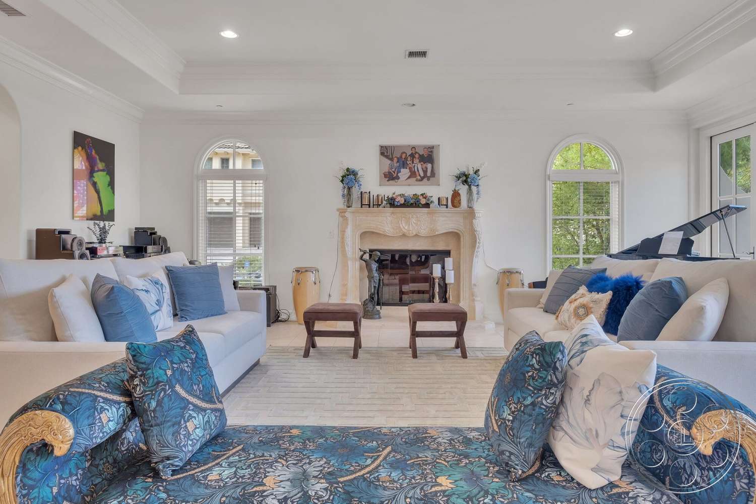 Medit 172 - light hardwood flooring, open floor plan, built-in shelving, blue decorative pillows, textured throw blanket, floral arrangements, plush fabric sofa, cozy living room, small accent table, white painted walls, artwork wall display, marble fireplace surround, crown molding details, arc-shaped windows, wooden side chairs