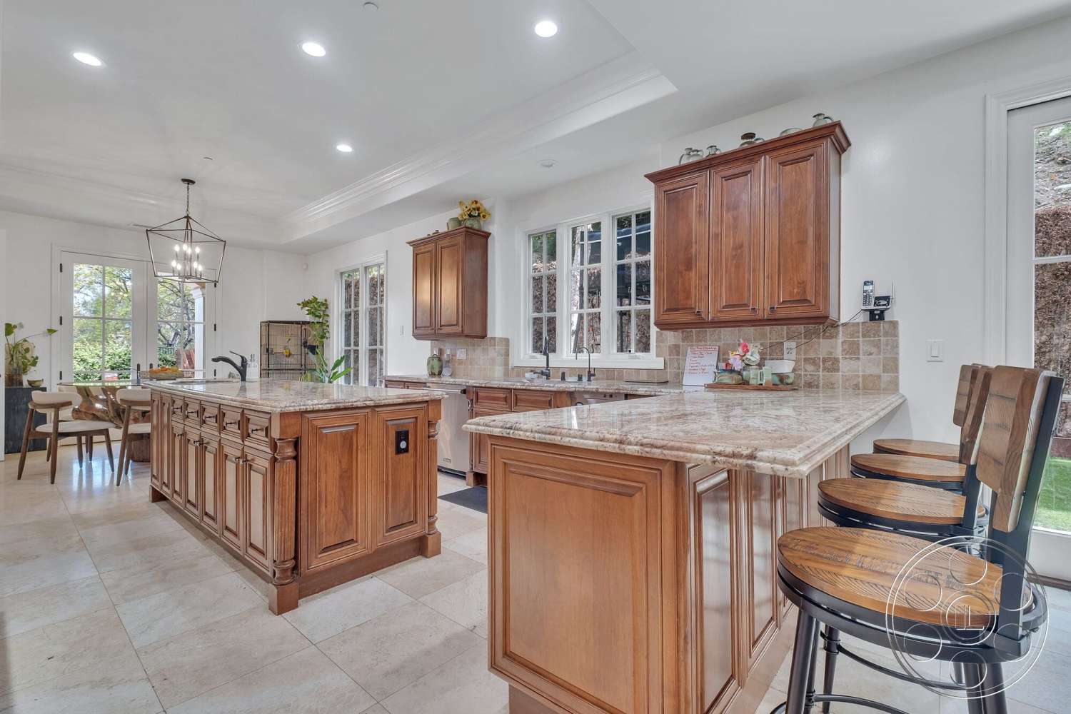 Medit 172 - open floor plan kitchen, dark wood kitchen cabinets, granite kitchen island countertop, cream-colored tile flooring, exposed wood light fixture, pantry door with glass panel, windowed wall with garden view, eat-in dining area, character-rich bar stool seating