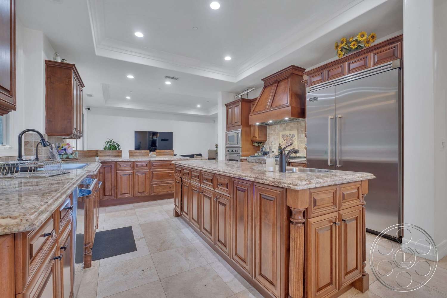 Medit 172 - dark wood cabinetry, light-colored walls, wall-mounted television, stainless steel appliances, undermount sink, decorative backsplash tiles, pantry area, granite kitchen countertops, open-concept kitchen design, crown molding details, bright interior lighting, island kitchen with seating, tile kitchen flooring, built-in kitchen oven