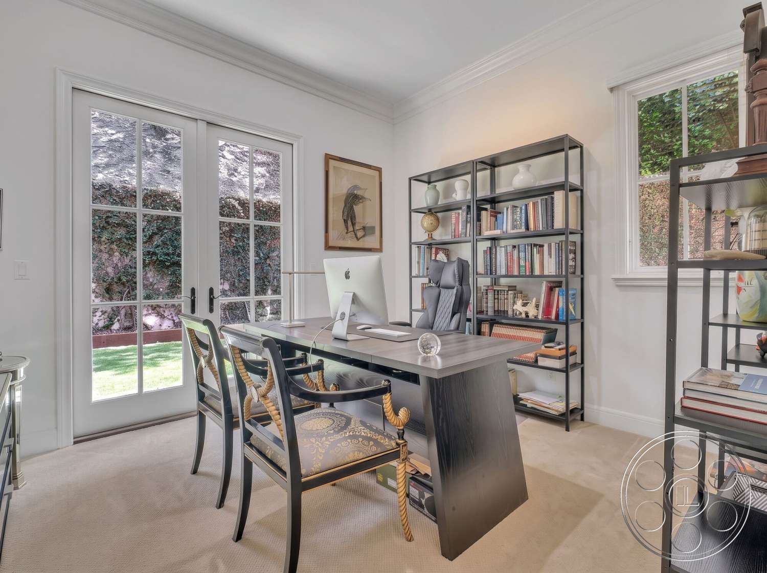 Medit 172 - exterior, carpet flooring, greenery visible through windows, natural light from large windows, ergonomic office chair, white painted walls, crown molding details, modern office design, framed artwork on walls, glass French doors, black desk with wood top, metal bookshelf with decorative objects