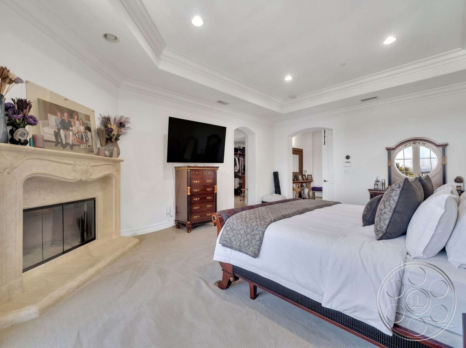 Medit 172 - floor-to-ceiling windows, textured ceiling, arched doorways, decorative throw pillows, large flat-screen television, dark wood dresser, elegant bedding, white painted walls, carpet bedroom flooring, framed family photographs, stone fireplace mantel