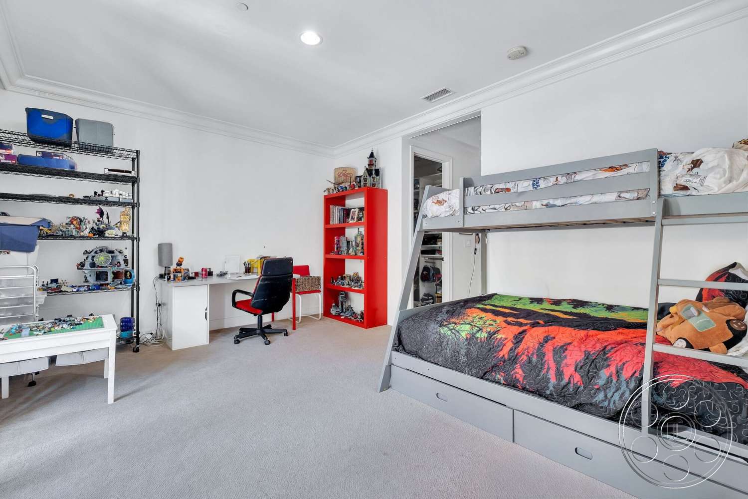 Medit 172 - minimalist decor, colorful patterned bedding, white painted walls, carpet bedroom flooring, bunk bed with gray metal frame, open shelving unit with multiple compartments, red accent storage shelves, desk with black ergonomic chair, small bedside lamp