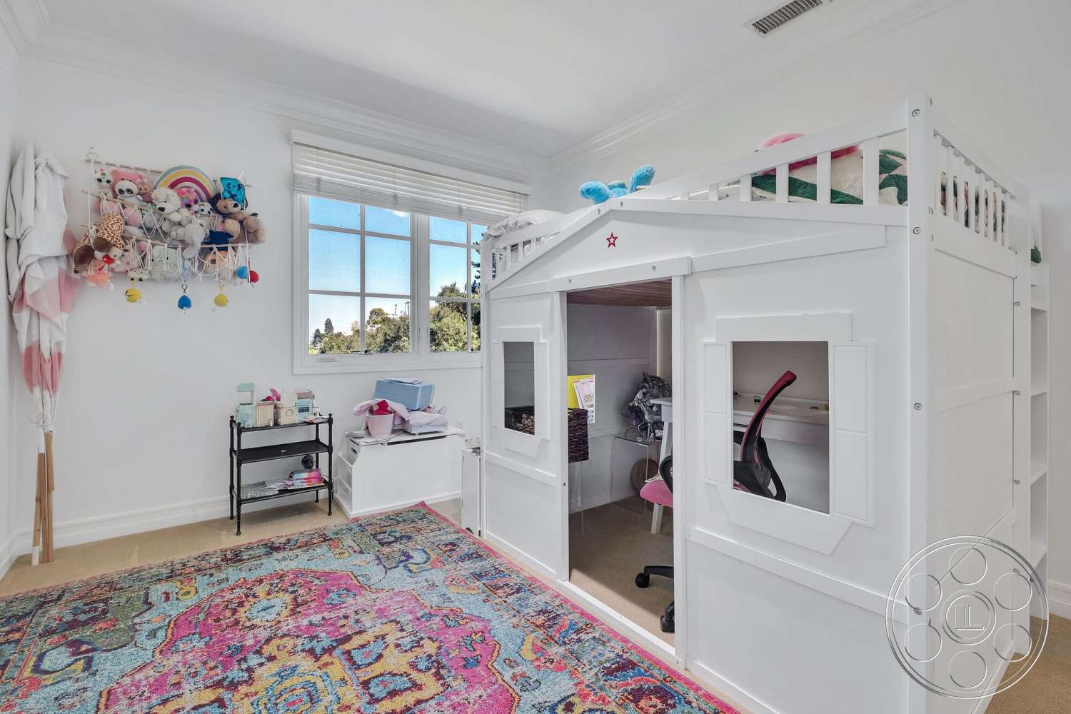 Medit 172 - white walls, colorful area rug, decorative plush toys, large rectangular windows, beige carpet flooring, lofted bed with playhouse design, wooden loft bed, black metal desk chair, white storage bins, shelving unit for toys, white wall-mounted toy storage, pink and blue color scheme