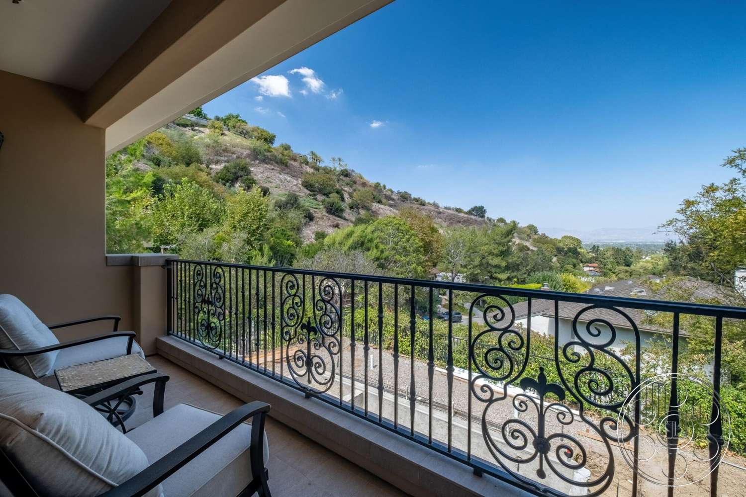 Medit 172 - mountain view, lush green landscaping, sunny outdoor setting, stucco wall finish, comfortable outdoor seating, exterior balcony railing, ornate wrought iron balcony railing, natural stone hillside, ceramic tile balcony floor, calm suburban environment