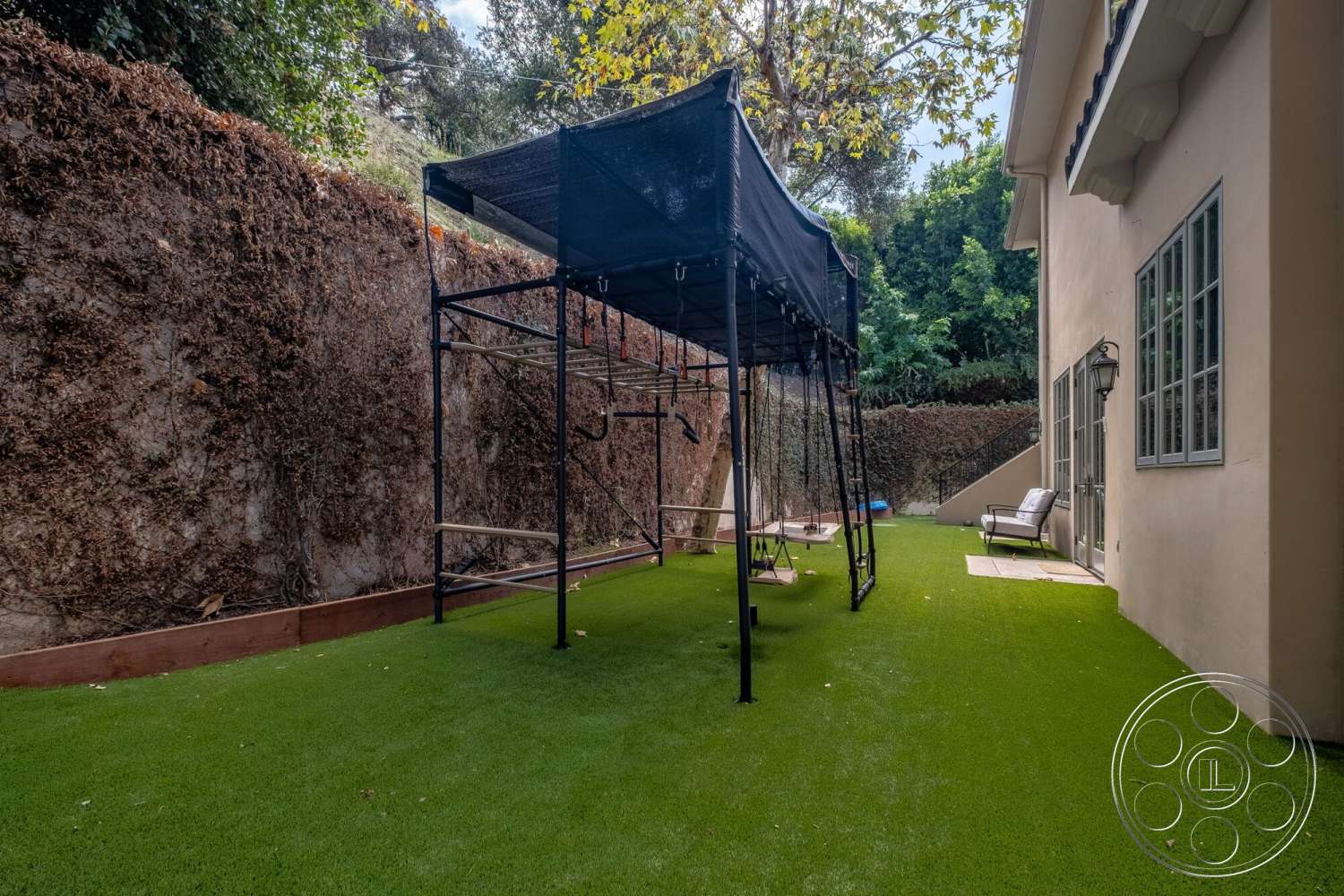 Medit 172 - exterior, landscaped hillside, patio seating area, artificial turf lawn, greenery backdrop, wooden border, metal playground structure, concrete side walkway, tan stucco wall, arched side windows