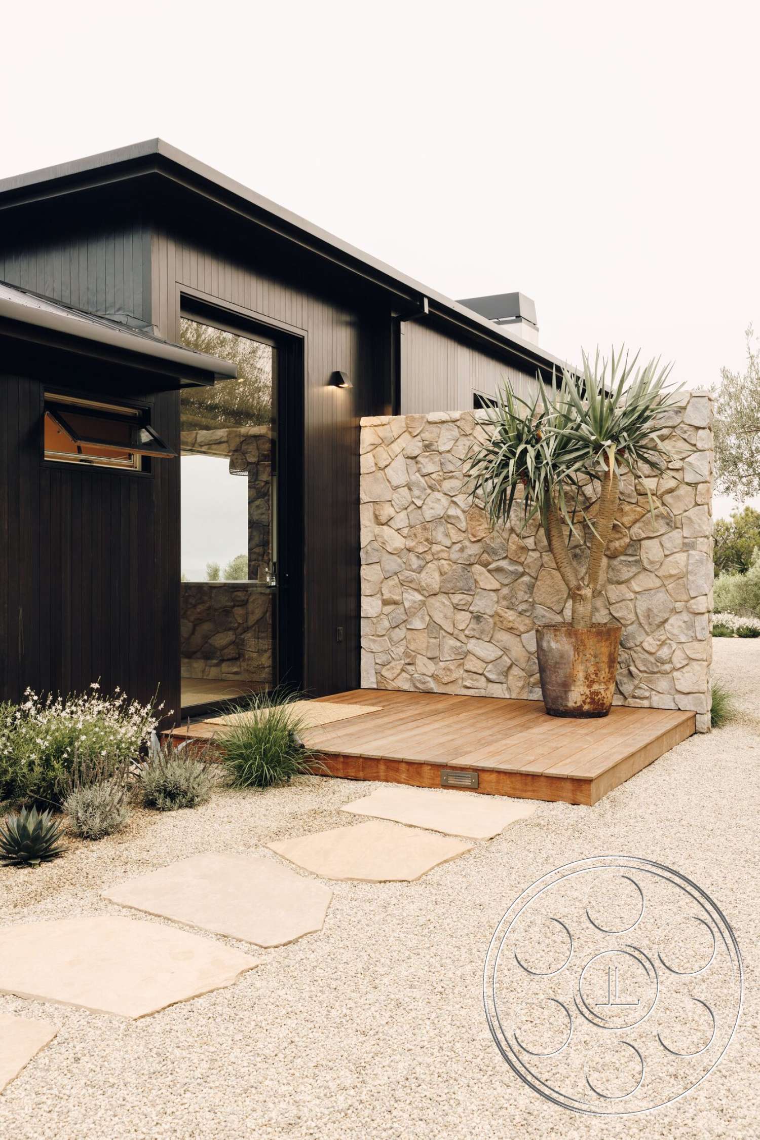 Modern 533 - exterior, modern architectural style, gravel landscaping, desert landscaping, contemporary aesthetic, natural stone wall, dark wood siding, large glass door, slate stepping stones, wooden deck porch