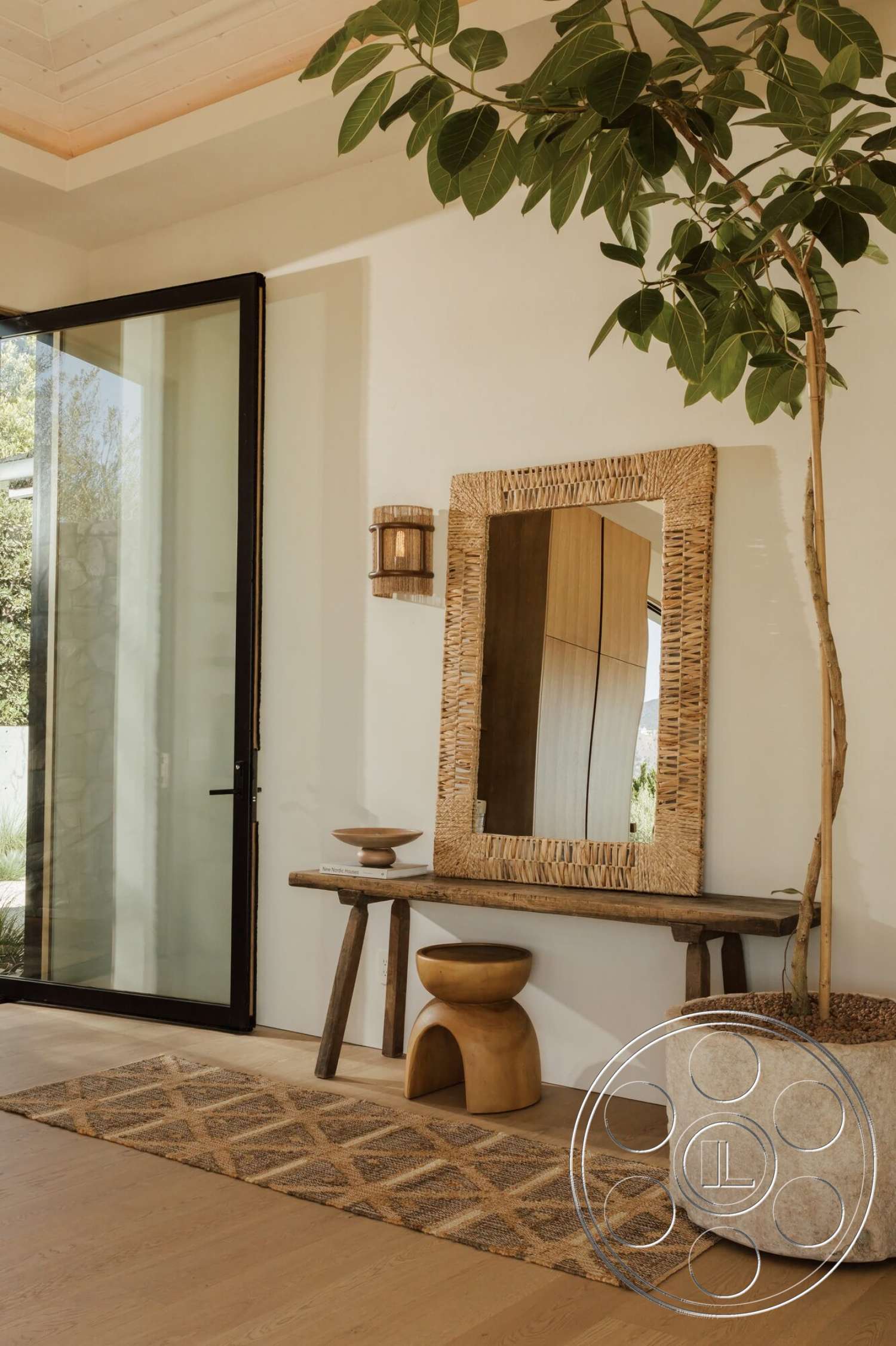 Modern 533 - natural wood flooring, wooden ceiling beams, glass entry door, concrete planter, area rug with geometric pattern, textured plaster wall, wood console table, wood accent stool, ceramic decorative bowl, indoor potted tree, woven wall mirror