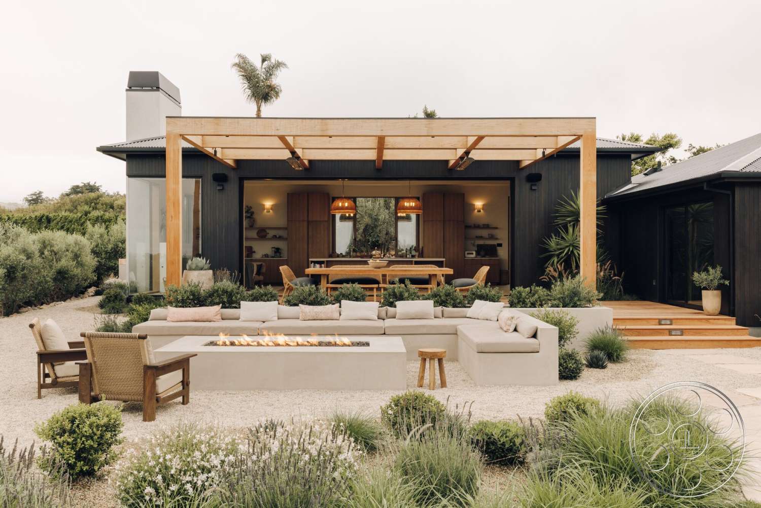 Modern 533 - exterior, glass sliding doors, exposed wooden beams, outdoor dining area, potted greenery, concrete seating area, wood pergola, landscaped garden area, modern ranch-style home, wood deck steps, low-maintenance foliage, concrete fire pit surround, textured gravel patio flooring, ceiling-mounted exterior lighting, neutral-toned outdoor cushions