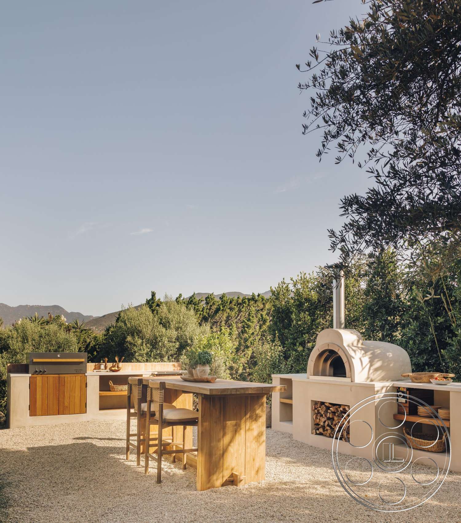 Modern 533 - exterior, mountain view, decorative potted plants, open-air setting, gravel patio flooring, wood outdoor dining table, wooden barstools, stucco outdoor kitchen cabinets, stone pizza oven, wooden storage compartment, varied greenery landscape
