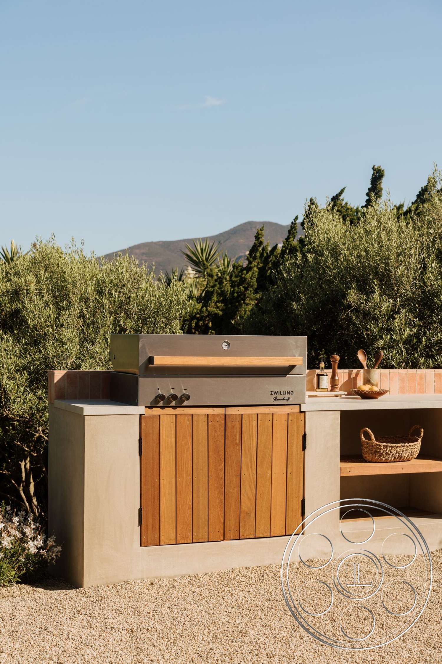 Modern 533 - exterior, stainless steel grill, ceramic tile backsplash, mountain view setting, gravel patio flooring, natural greenery backdrop, concrete outdoor kitchen base, wooden cabinetry doors, textured plaster countertop