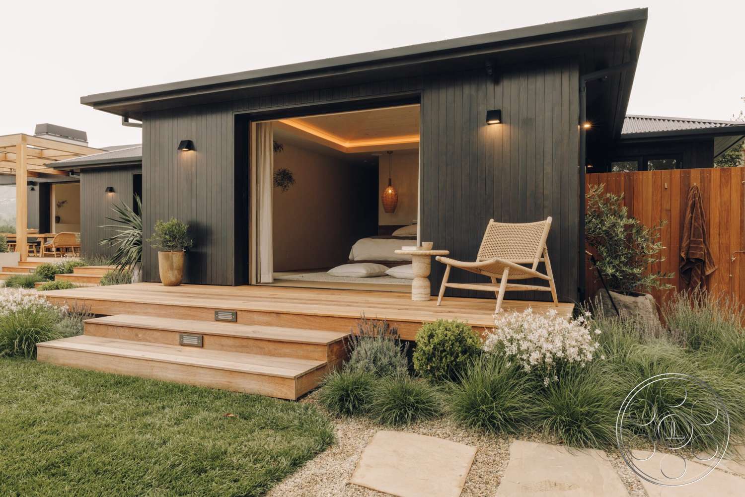 Modern 533 - exterior, landscaped garden, modern outdoor furniture, wooden steps, lush green grass, concrete stepping stones, simple geometric forms, planter with ornamental grass, dark wood vertical siding, outdoor accent lighting, natural wood contrast