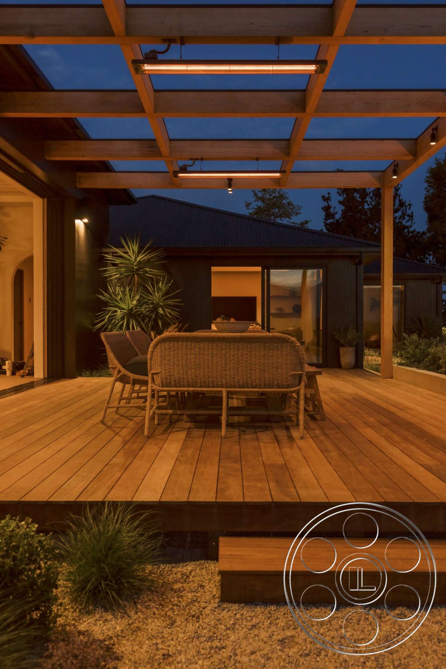 Modern 533 - exterior, floor-to-ceiling windows, ambient outdoor lighting, modern home design, landscaped garden setting, wood deck flooring, woven outdoor dining chairs, gravel garden border, cedar wood pergola