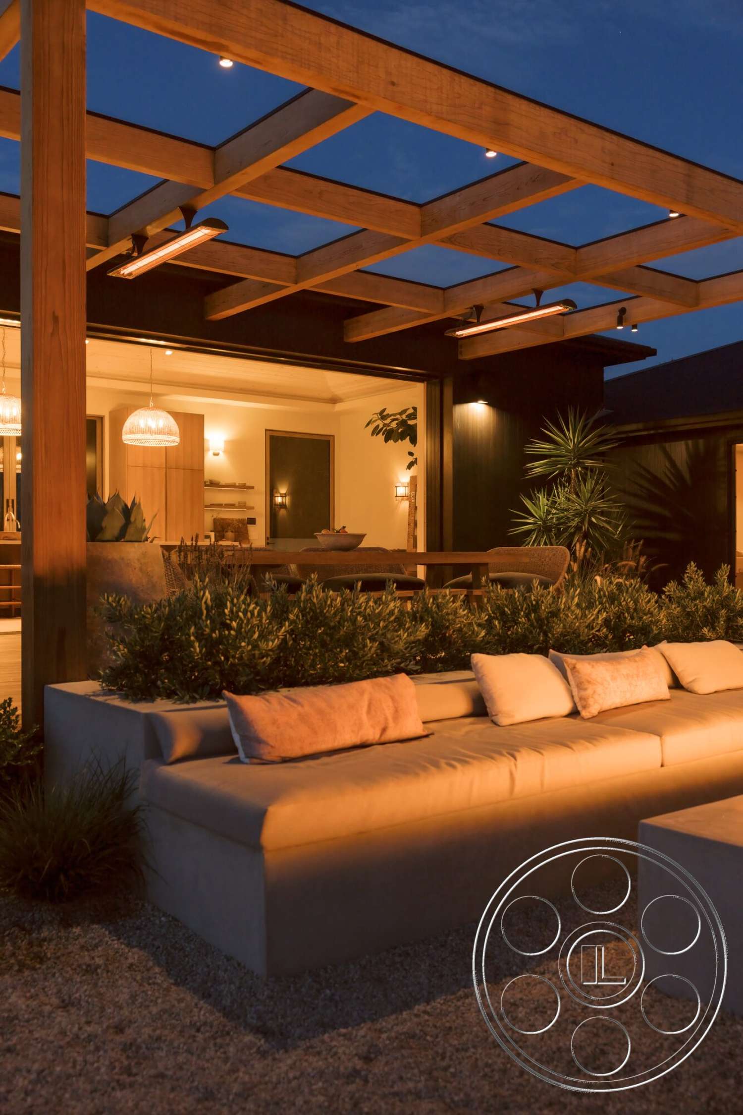 Modern 533 - exterior, floor-to-ceiling windows, nighttime illumination, landscaped garden area, wood pergola structure, gravel patio flooring, modern home aesthetic, interior open layout, concrete built-in seating, decorative pillow accents