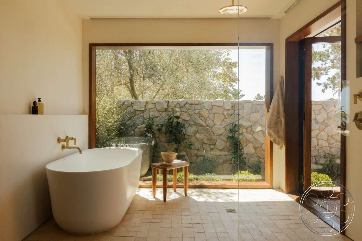 Modern 533 - large windows, freestanding bathtub, glass shower enclosure, brass fixtures, textured plaster walls, natural stone wall, interior bathroom, outdoor greenery view, neutral tile flooring, natural wood stool, wood door frame