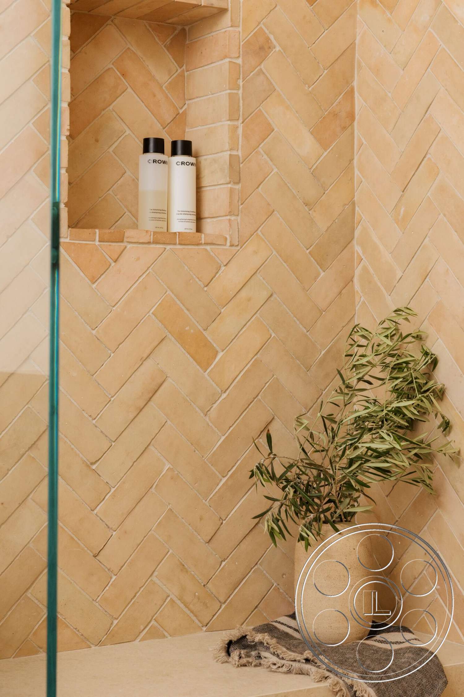 Modern 533 - minimalist aesthetic, glass shower door, built-in shower niche, ceramic vase with greenery, herringbone pattern tile walls, terracotta tile shower walls, natural stone shower shelf, soft textile bath mat