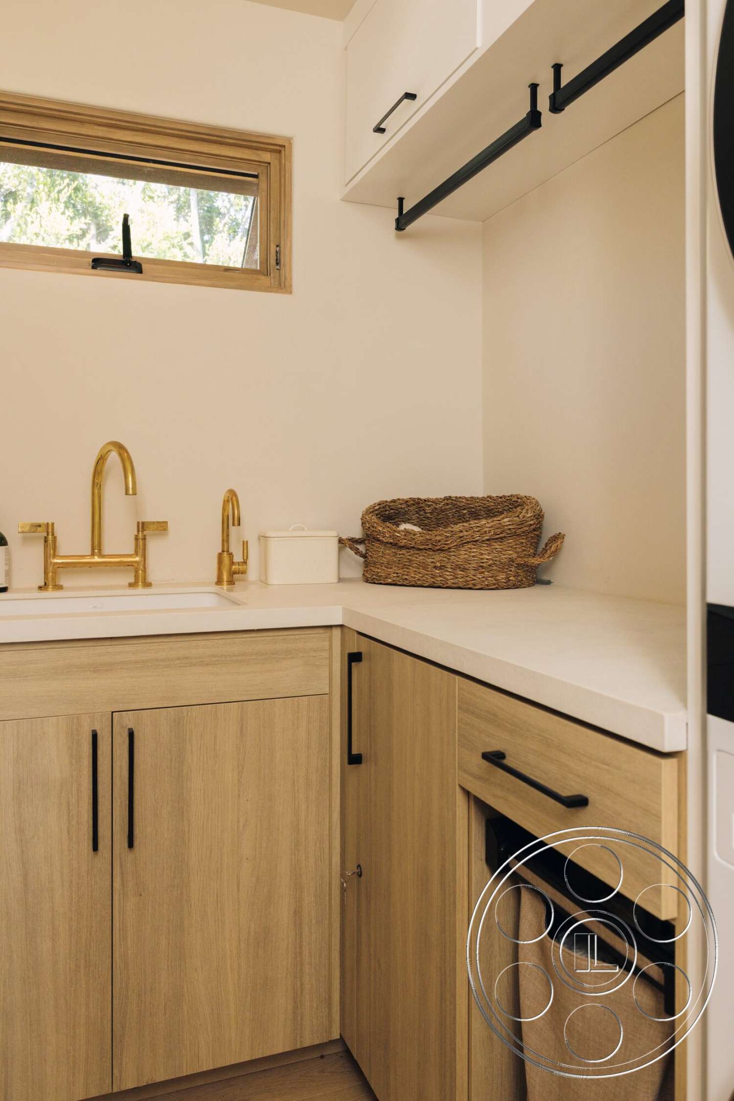 Modern 533 - light wood cabinetry, white quartz countertop, textured beige walls, integrated appliance design, woven basket storage, small rectangular window, brushed gold faucet, black handle hardware