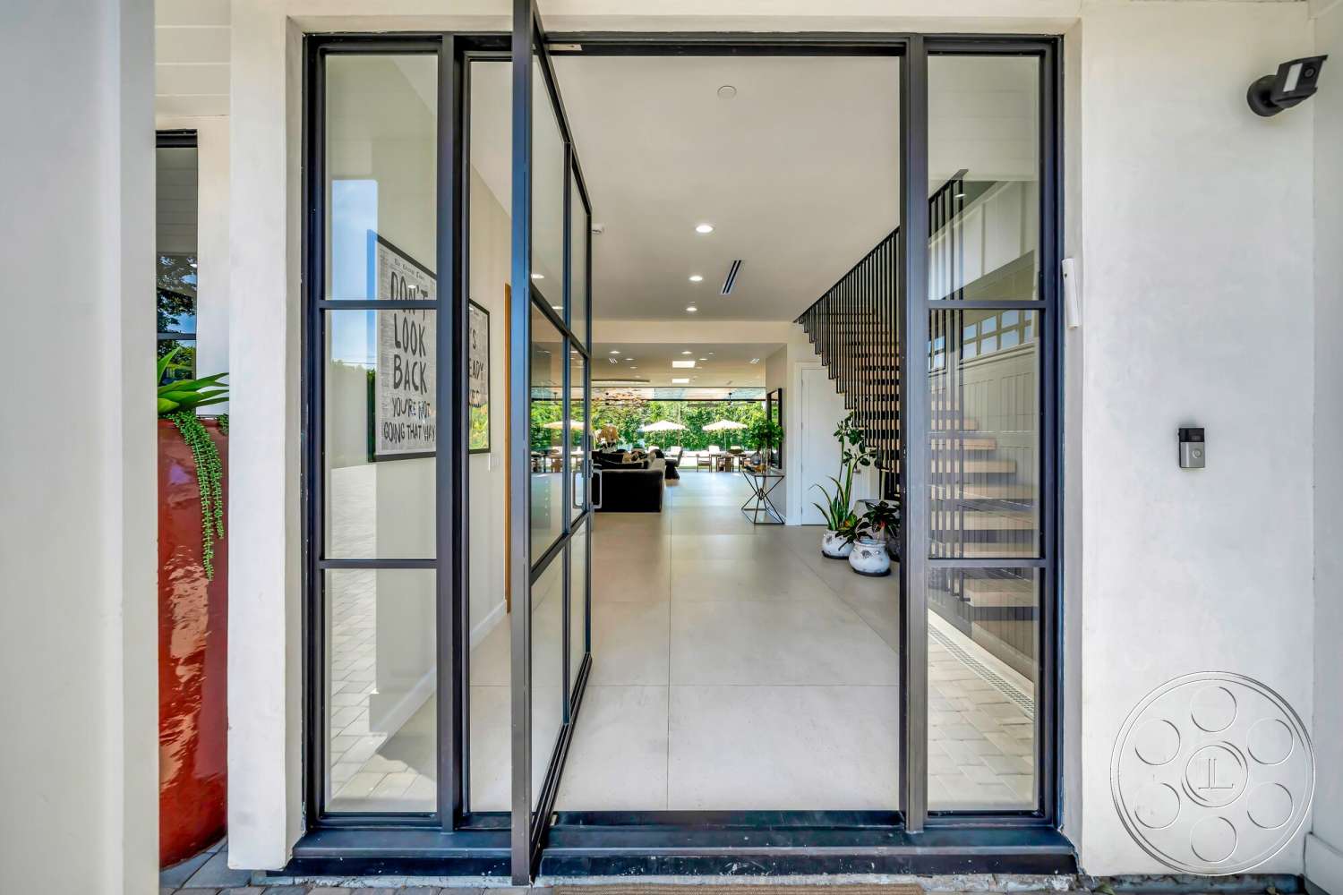 Modern 534 - open floor plan, decorative wall art, vaulted ceiling, bright natural lighting, outdoor view, textured wall finishes, large potted plants, stone tile flooring, contemporary architectural style, exterior entrance, glass double doors, interior foyer, modern staircase with wooden treads, black metal frame windows, view into living area