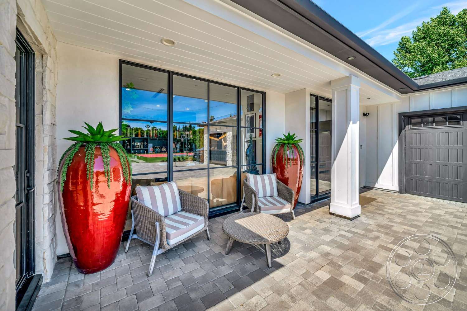 Modern 534 - exterior, stone feature wall, sloped roofline, paver patio flooring, modern glass windows, curved entryway design, natural landscaping view, white horizontal siding, decorative outdoor furniture, contemporary porch seating, red ceramic planters, bright sunlight illumination