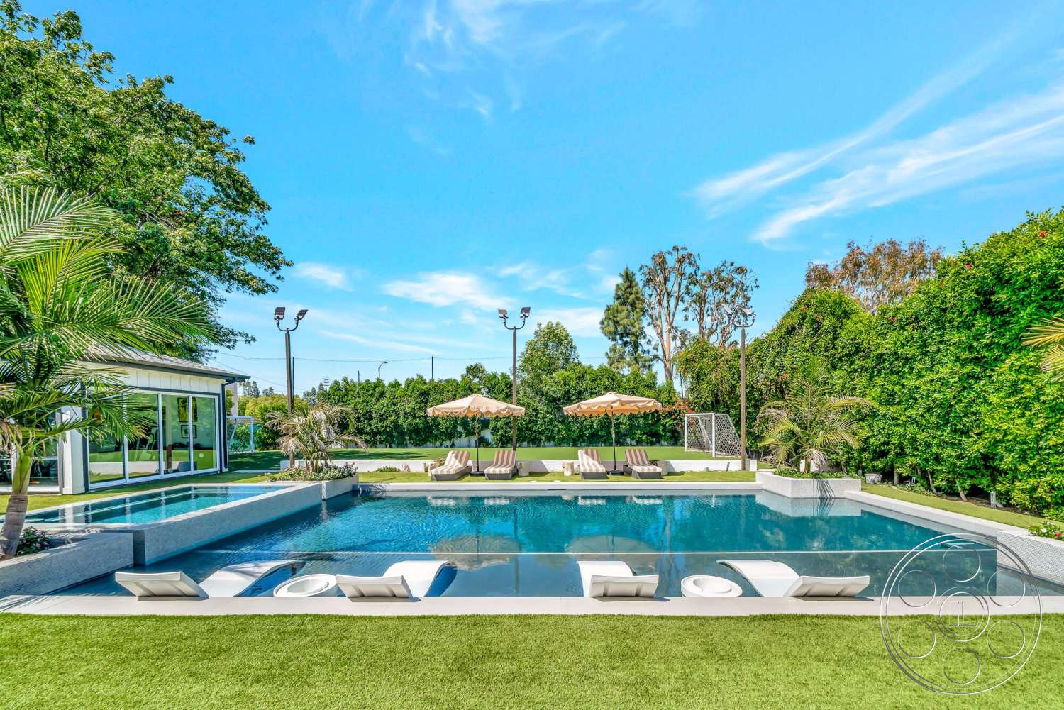 Modern 534 - exterior, landscaped garden, modern architecture, outdoor seating area, sun loungers, infinity pool, tropical palm trees, concrete pool deck, fenced yard, sports field, bright blue sky, patio umbrellas, expansive glass windows, tranquil outdoor space, turf lawn, glass pool walls, step stone walkways