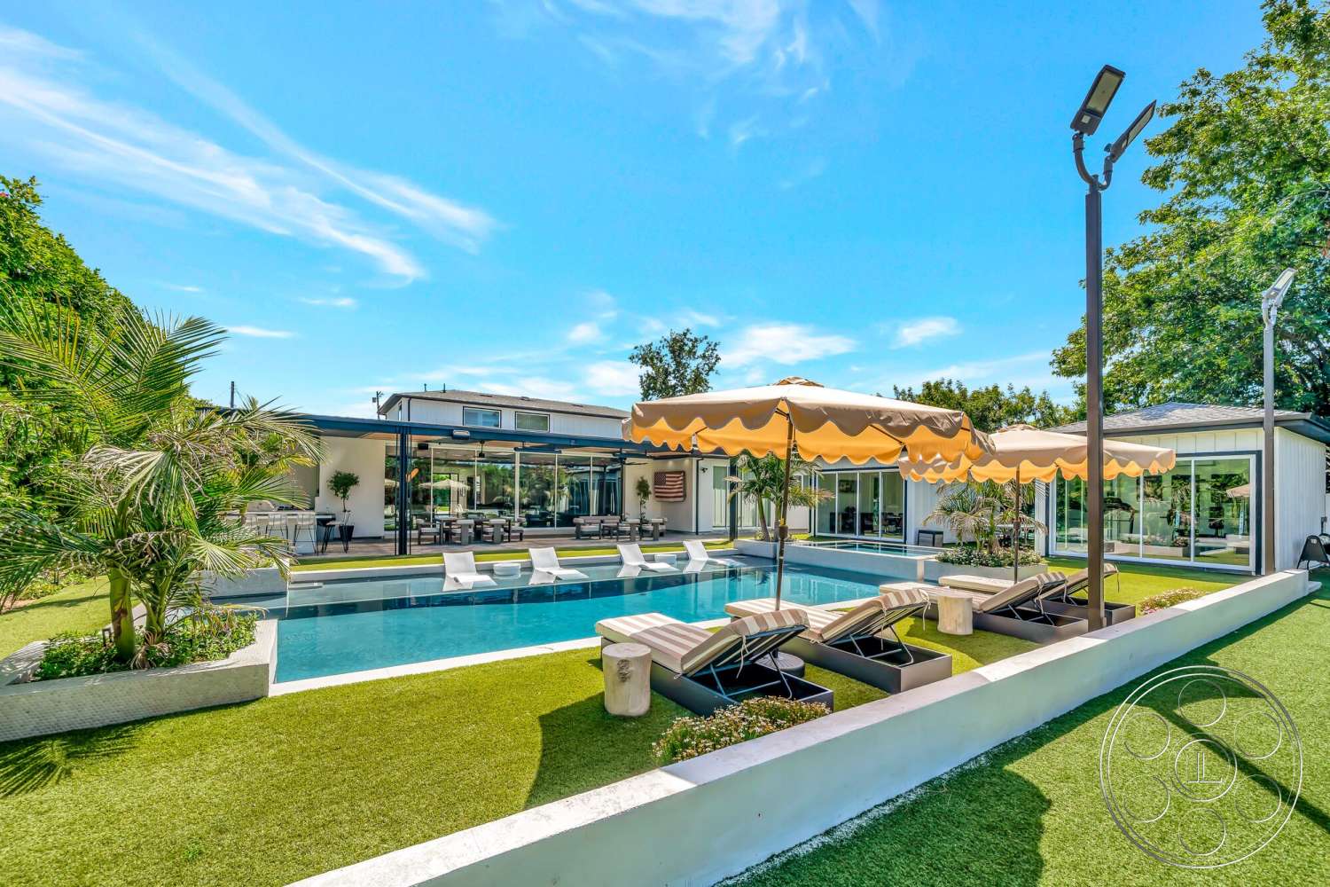 Modern 534 - exterior, glass sliding doors, outdoor seating area, rectangular swimming pool, lawn area, artificial grass landscaping, white concrete walls, sunny outdoor space, urban backyard, modern residential architecture, open-air layout, concrete pool border, tropical palm landscaping, metal patio lounge chairs, fabric sun umbrellas, poolside terrace