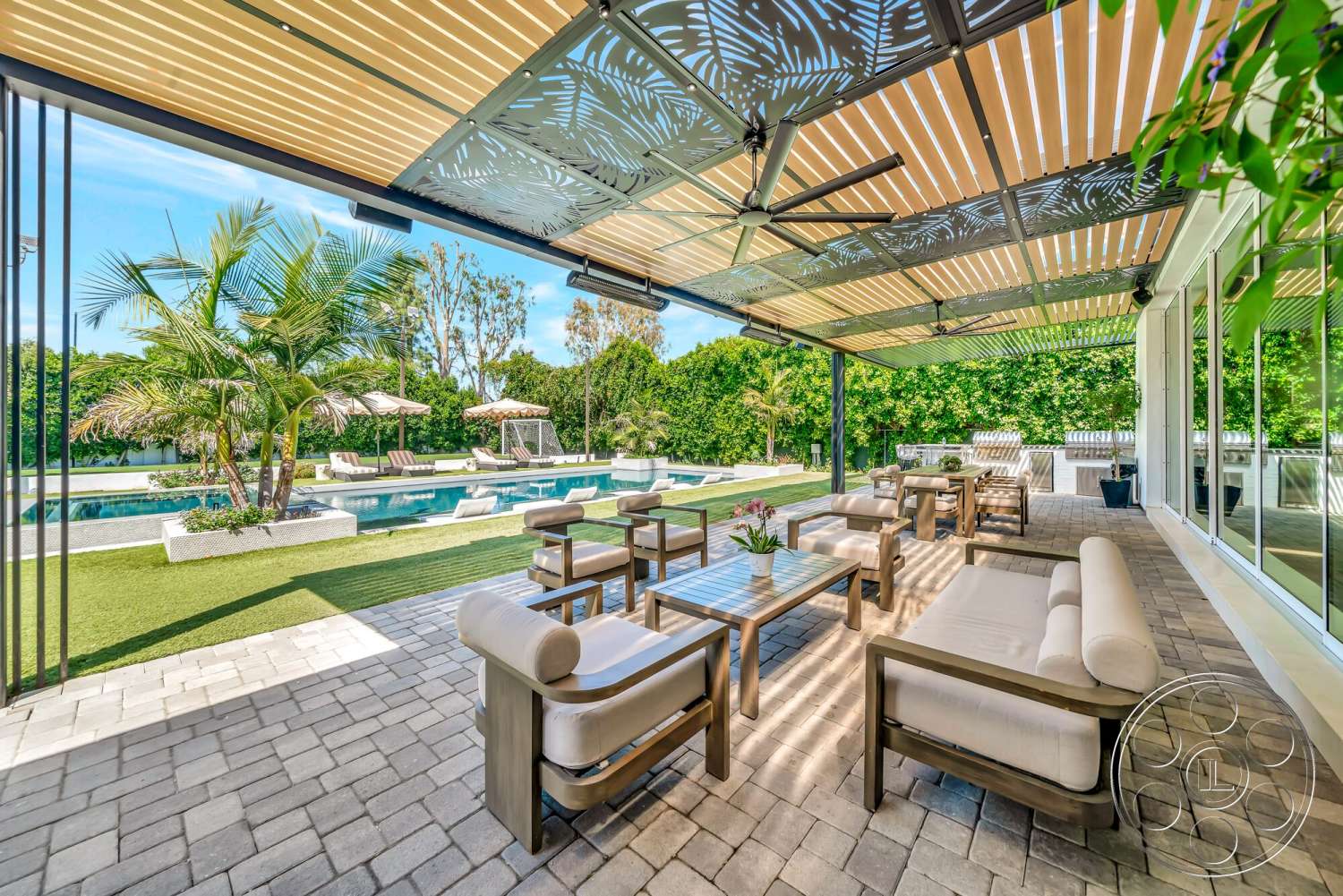 Modern 534 - exterior, wooden coffee table, glass sliding doors, modern outdoor furniture, single-story home, outdoor lounge area, open-air design, rectangular pool, concrete pool border, lush greenery landscaping, paver patio flooring, synthetic grass lawn, aluminum pergola with decorative metal panels, sectional outdoor sofa with fabric cushions, palms and umbrellas